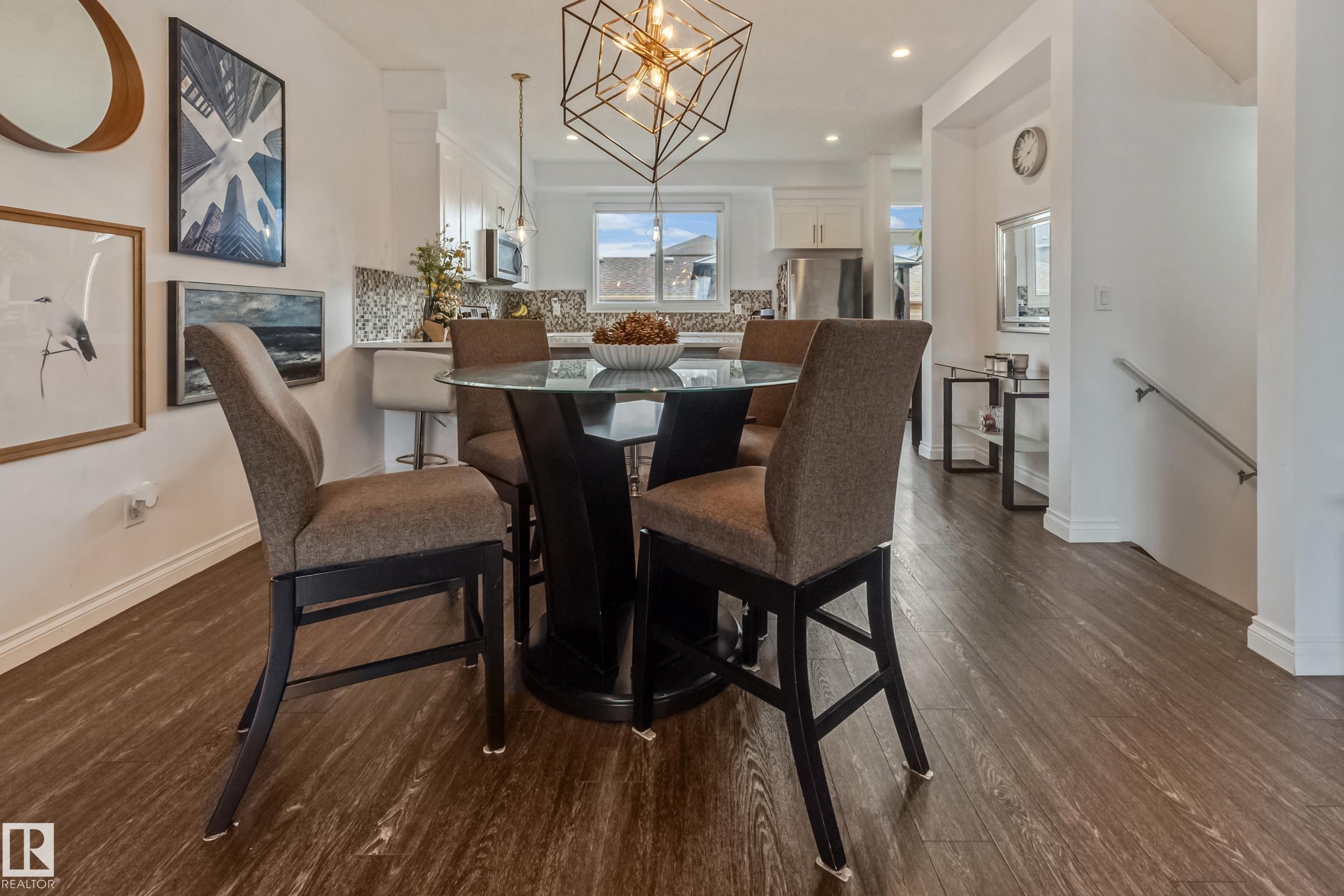 Open-concept dining area featuring wood-finish flooring, a contemporary overhead light fixture, and a kitchen with white cabinetry - 8131 Chappelle Way, Edmonton, AB - Indoor Photo Showing Dining Room