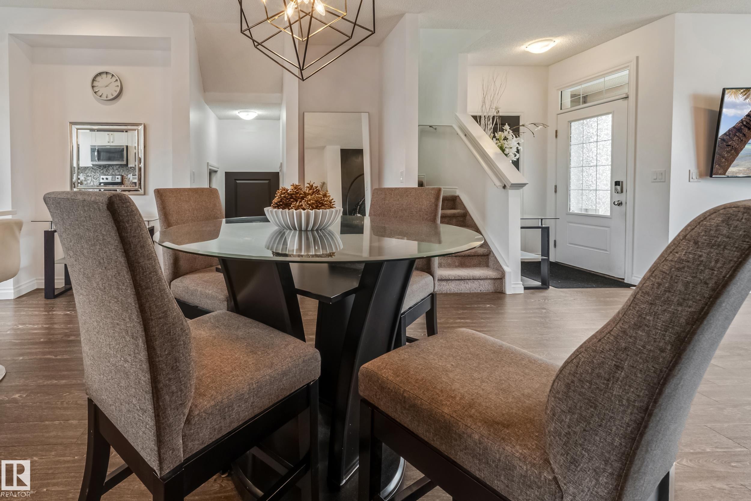 Open-concept living space featuring wood-finish flooring, a white paneled entrance door with textured glass inserts, and a contemporary geometric chandelier - 8131 Chappelle Way, Edmonton, AB - Indoor Photo Showing Dining Room