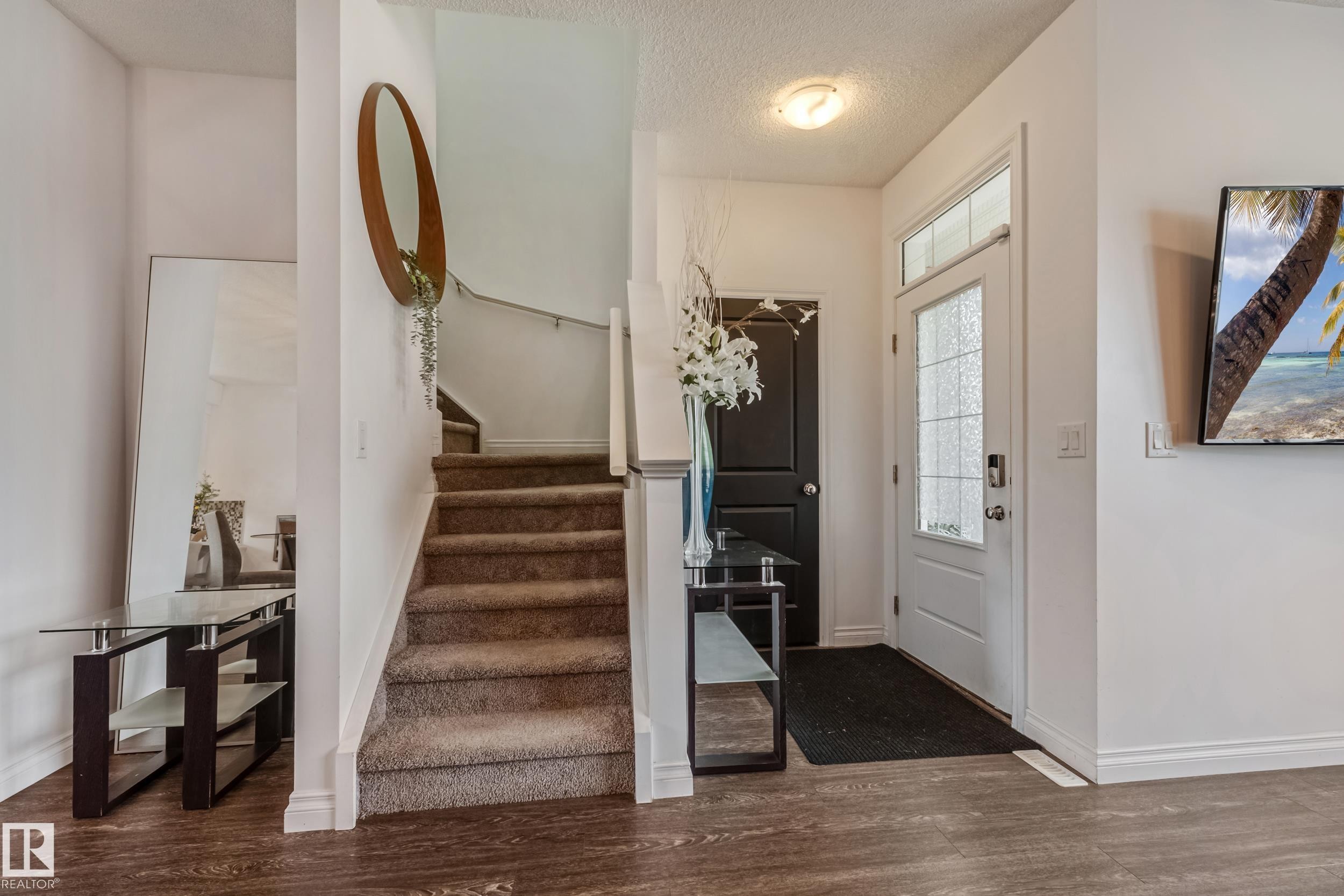 Entryway featuring wood-finish flooring, a carpeted staircase with a white railing, and a white paneled door with decorative glass inserts and a transom window - 8131 Chappelle Way, Edmonton, AB - Indoor Photo Showing Other Room