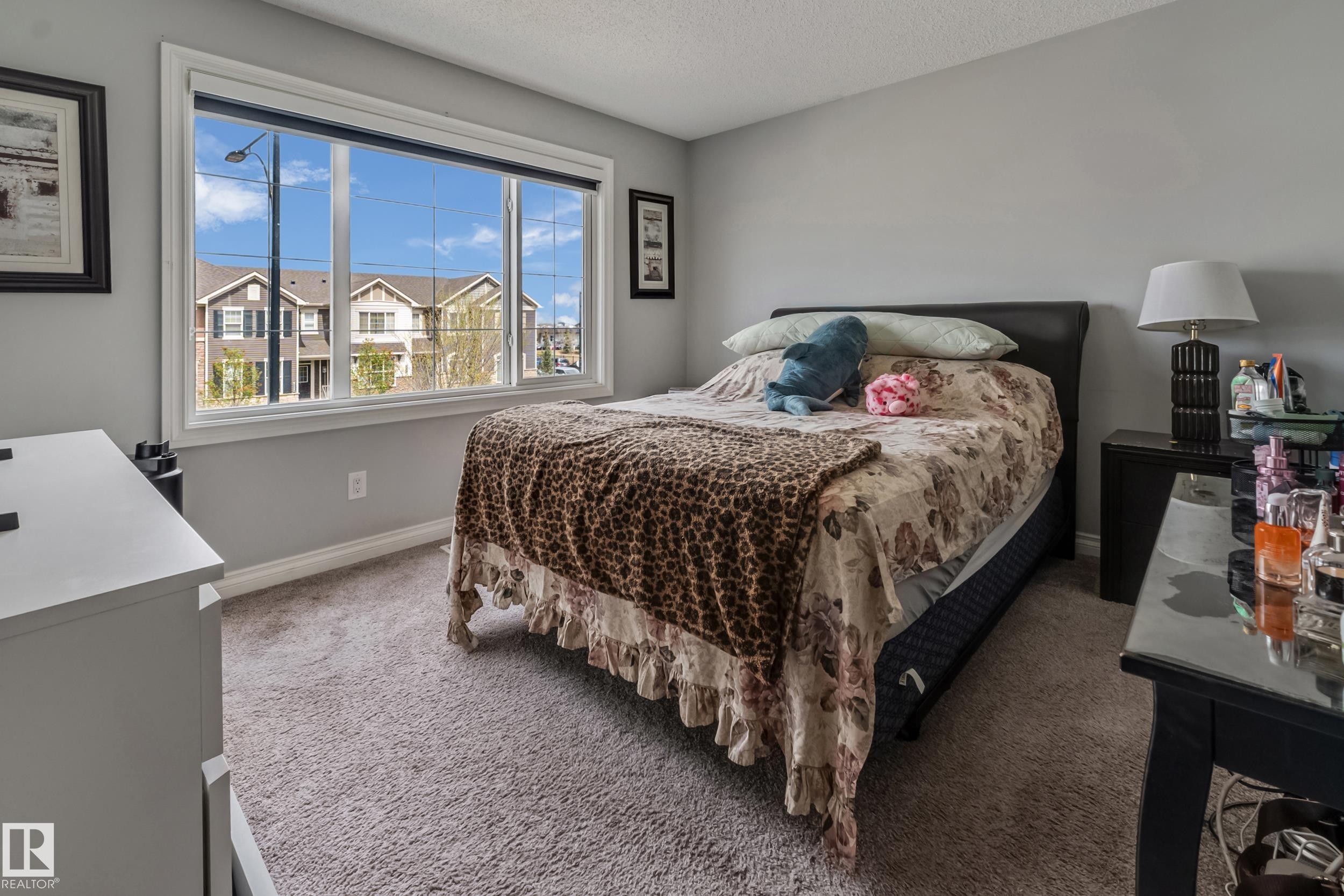 Neutral-toned room featuring a large window with white trim, light gray painted walls, and textured carpet flooring - 8131 Chappelle Way, Edmonton, AB - Indoor Photo Showing Bedroom