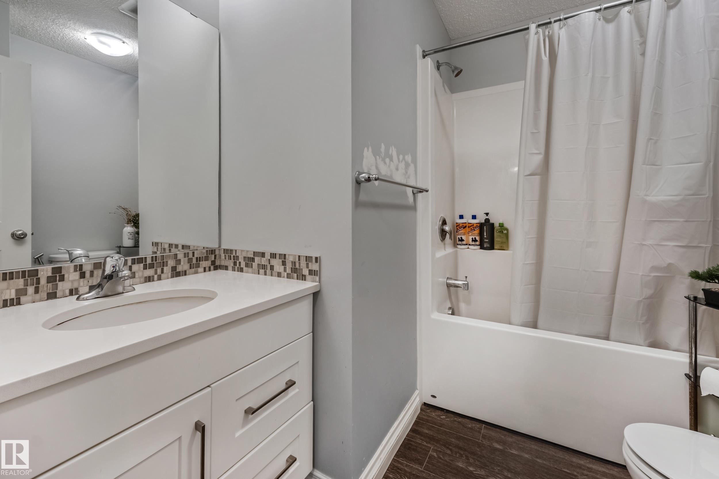 Bathroom featuring a white vanity with an undermount sink, mosaic tile backsplash, and a shower/tub combination with a white surround - 8131 Chappelle Way, Edmonton, AB - Indoor Photo Showing Bathroom