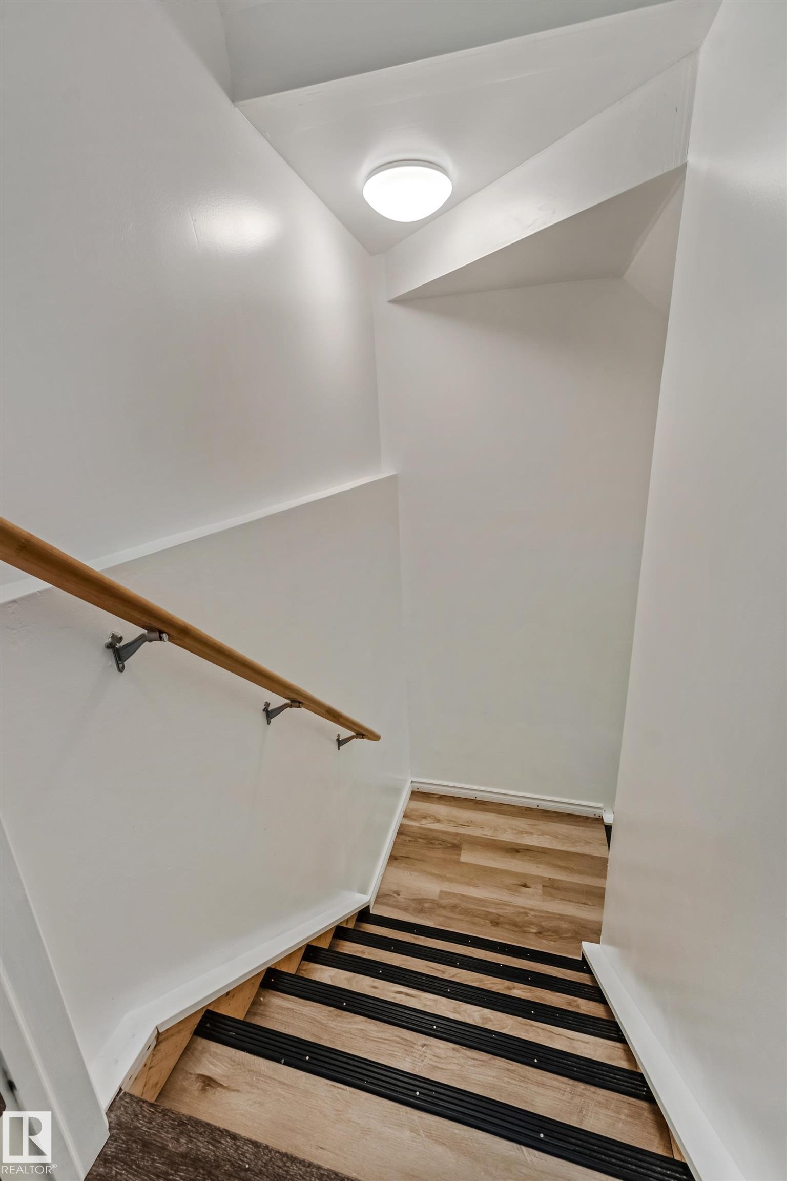 Staircase featuring wood-finish treads with black anti-slip strips, a light wood handrail with metal brackets, white painted walls, and an overhead flush-mount light fixture - 8131 Chappelle Way, Edmonton, AB - Indoor Photo Showing Other Room