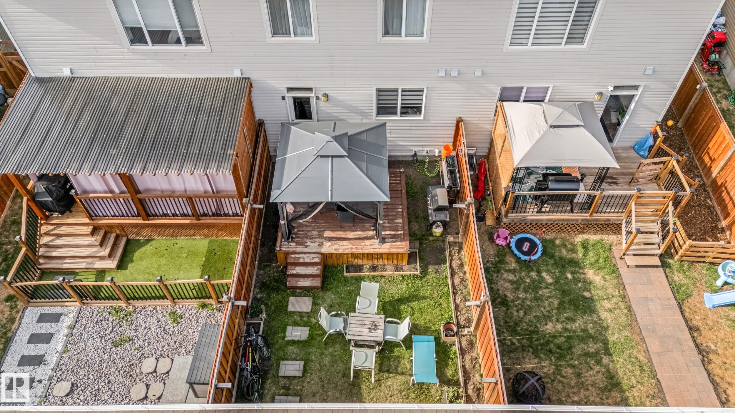 Rear exterior showcasing a multi-level wood deck with a covered area, artificial turf, and a gravel patio with stepping stones - 8131 Chappelle Way, Edmonton, AB - Outdoor With Exterior
