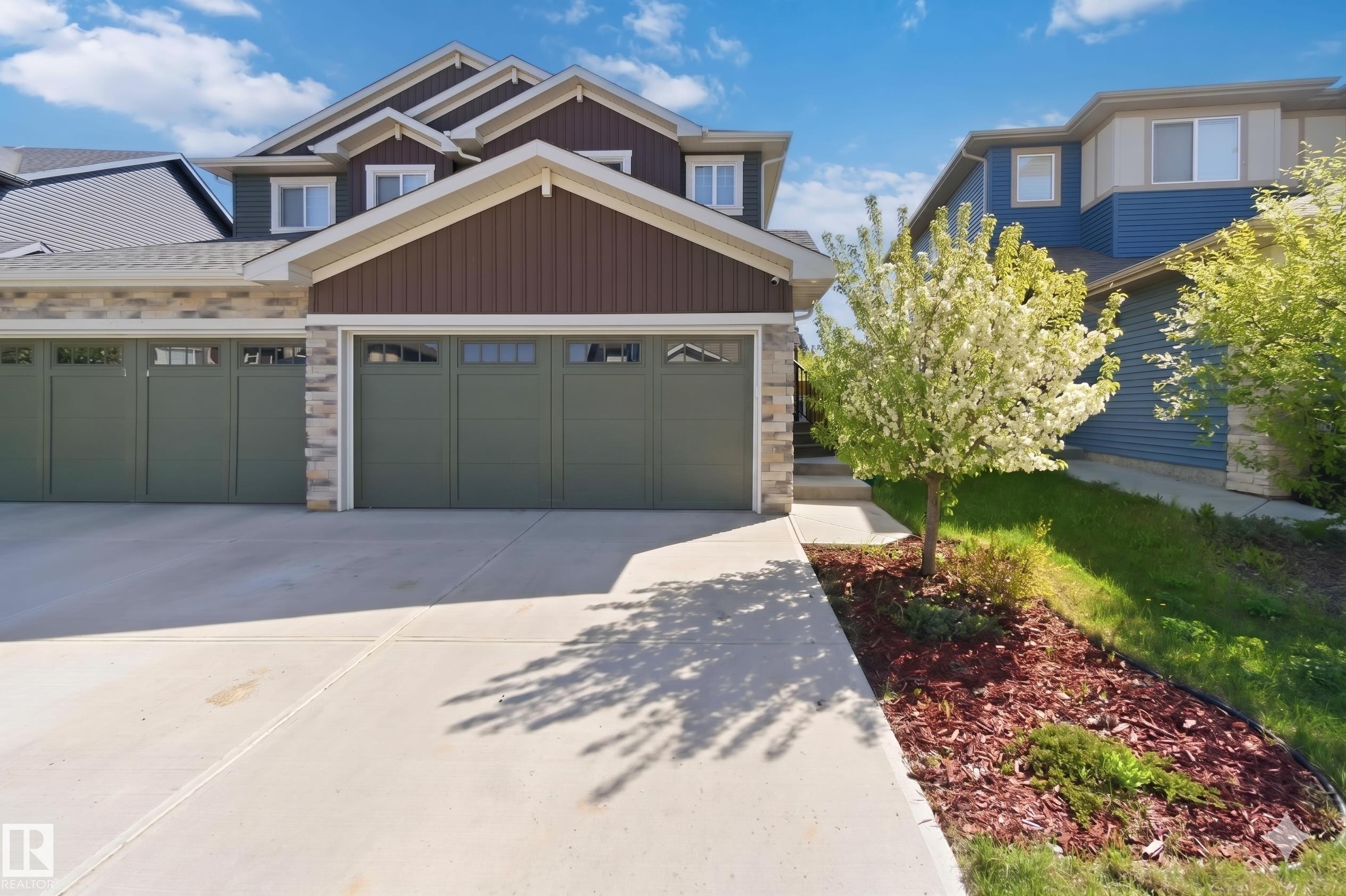 Exterior featuring a three-car garage with green doors and transom windows, a concrete driveway, stone facade accents, and brown vertical siding - 5129 Lark Crescent, Edmonton, AB - Outdoor
