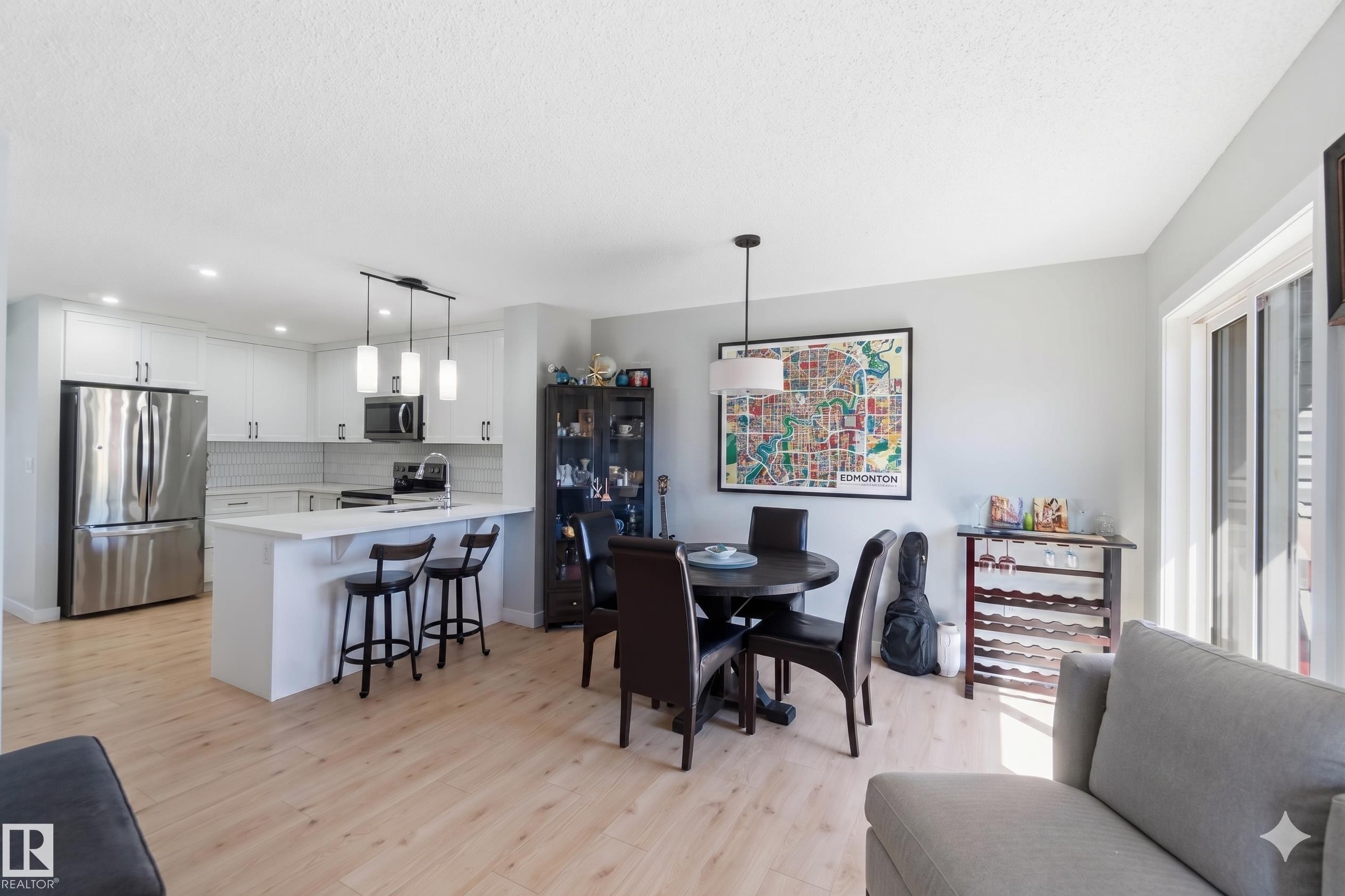 Open-concept kitchen and dining area featuring light wood-finish flooring, white cabinetry, stainless steel appliances, a kitchen island with seating, and a sliding glass door - 5129 Lark Crescent, Edmonton, AB - Indoor