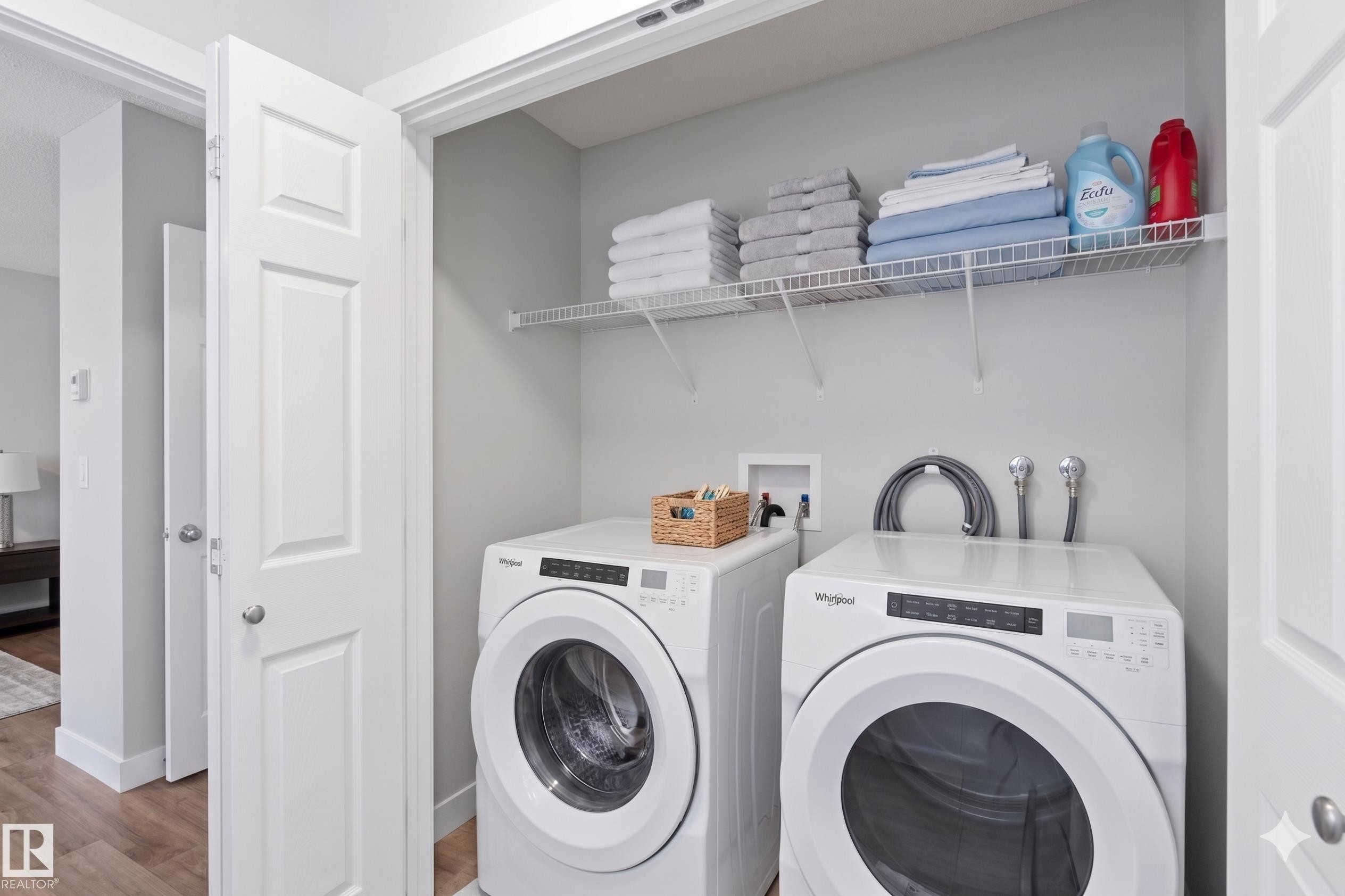 Dedicated laundry closet featuring a stacked washer and dryer, wire shelving, and light wood-finish flooring - 5129 Lark Crescent, Edmonton, AB - Indoor Photo Showing Laundry Room