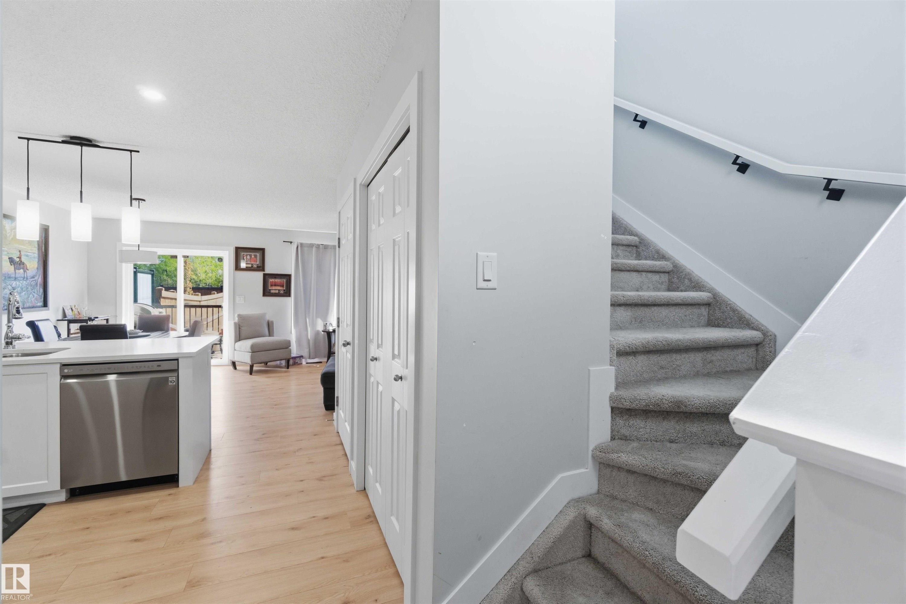 Open-concept living area featuring wood-finish flooring, white cabinetry, a stainless steel dishwasher, and a contemporary linear pendant light fixture - 5129 Lark Crescent, Edmonton, AB - Indoor