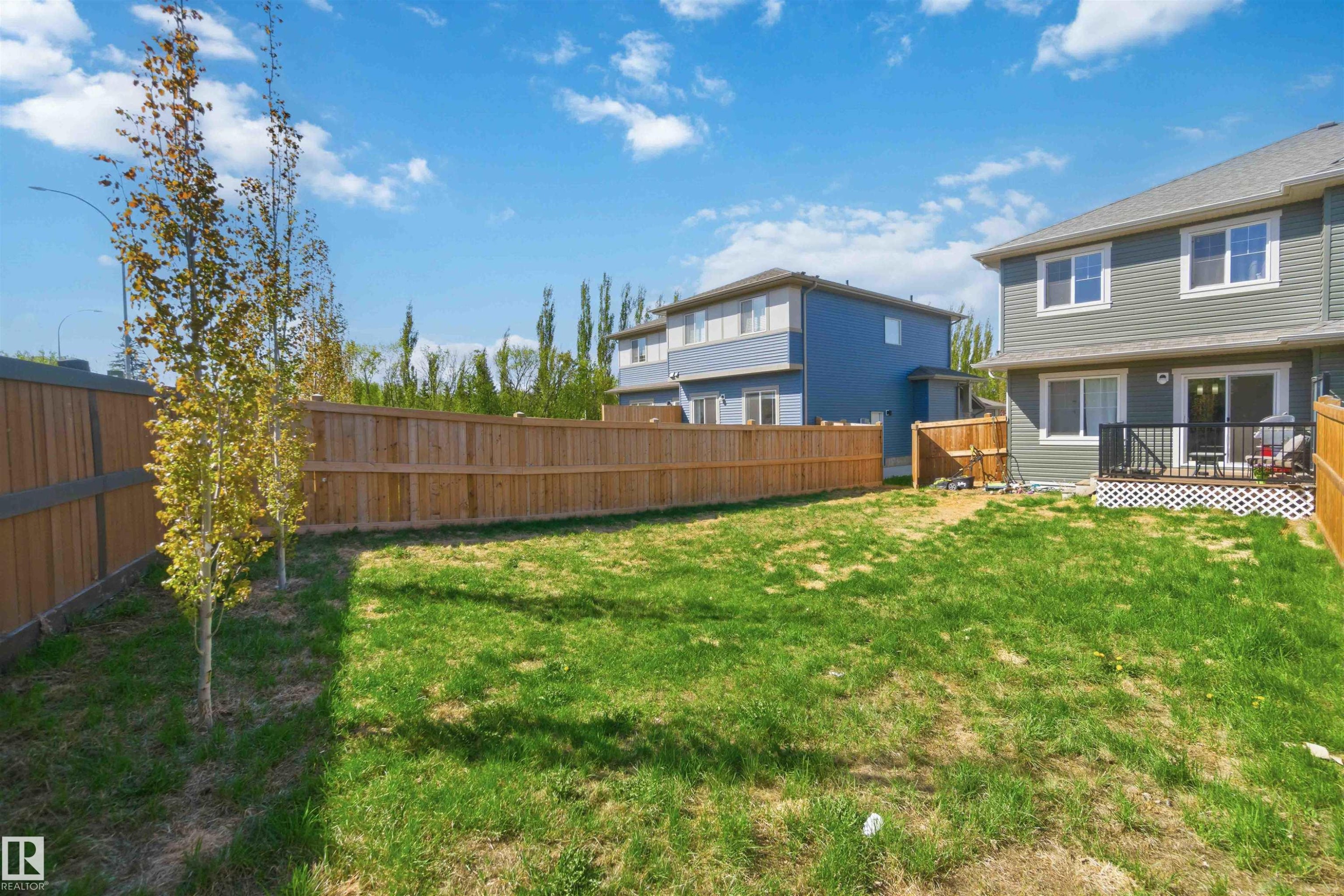 Expansive grassy backyard featuring a full wood privacy fence and a ground-level deck with black railings - 5129 Lark Crescent, Edmonton, AB - Outdoor With Deck Patio Veranda