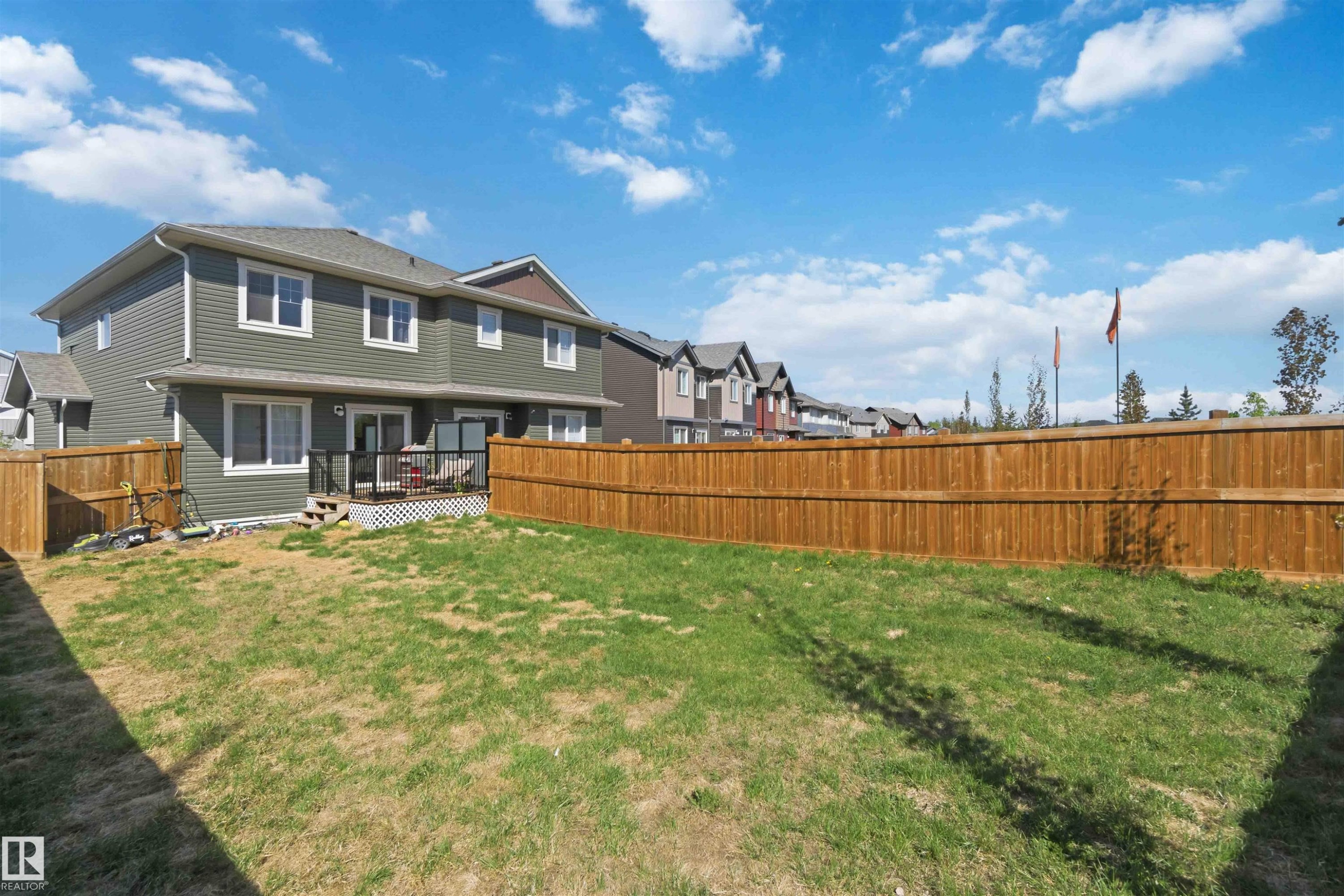 Fenced backyard featuring a wood deck with glass railing, green lawn, and panel siding exterior - 5129 Lark Crescent, Edmonton, AB - Outdoor With Deck Patio Veranda