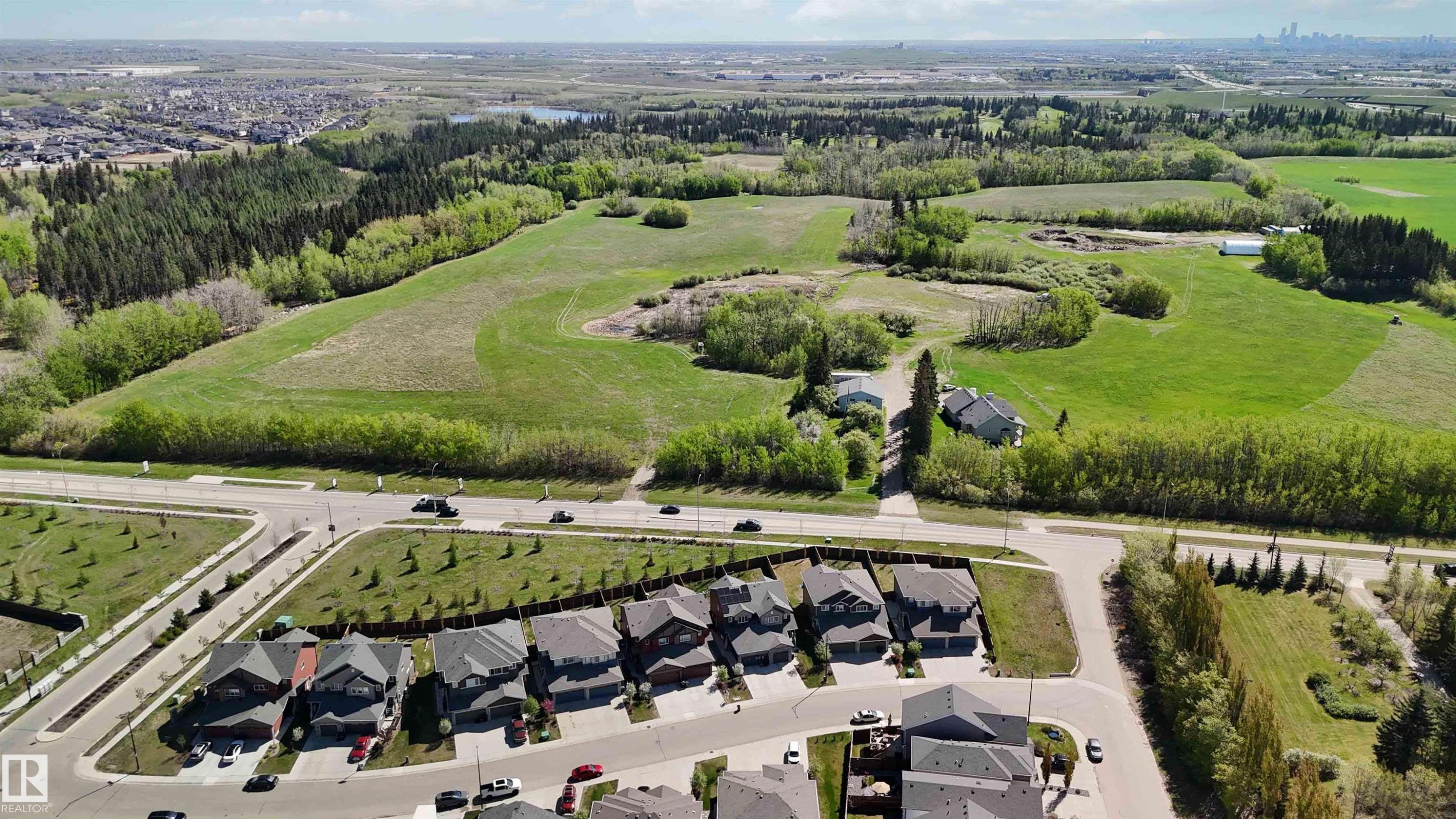 Aerial perspective showcasing a residential development bordering expansive green fields and mature tree lines - 5129 Lark Crescent, Edmonton, AB - Outdoor With View