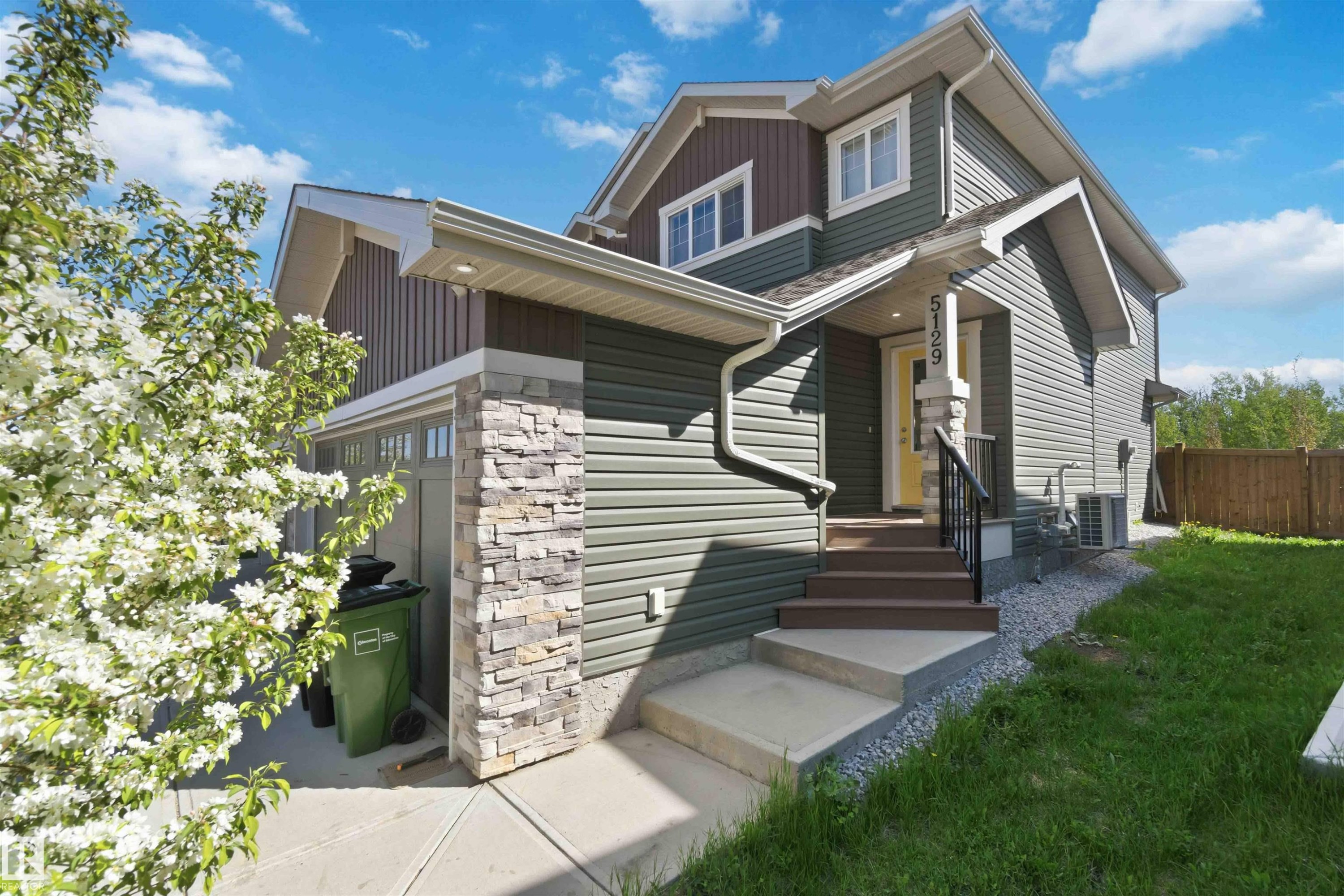Contemporary home exterior featuring horizontal siding in shades of green and brown, stone veneer accents, white trim, and a prominent front entrance with a yellow door - 5129 Lark Crescent, Edmonton, AB - Outdoor