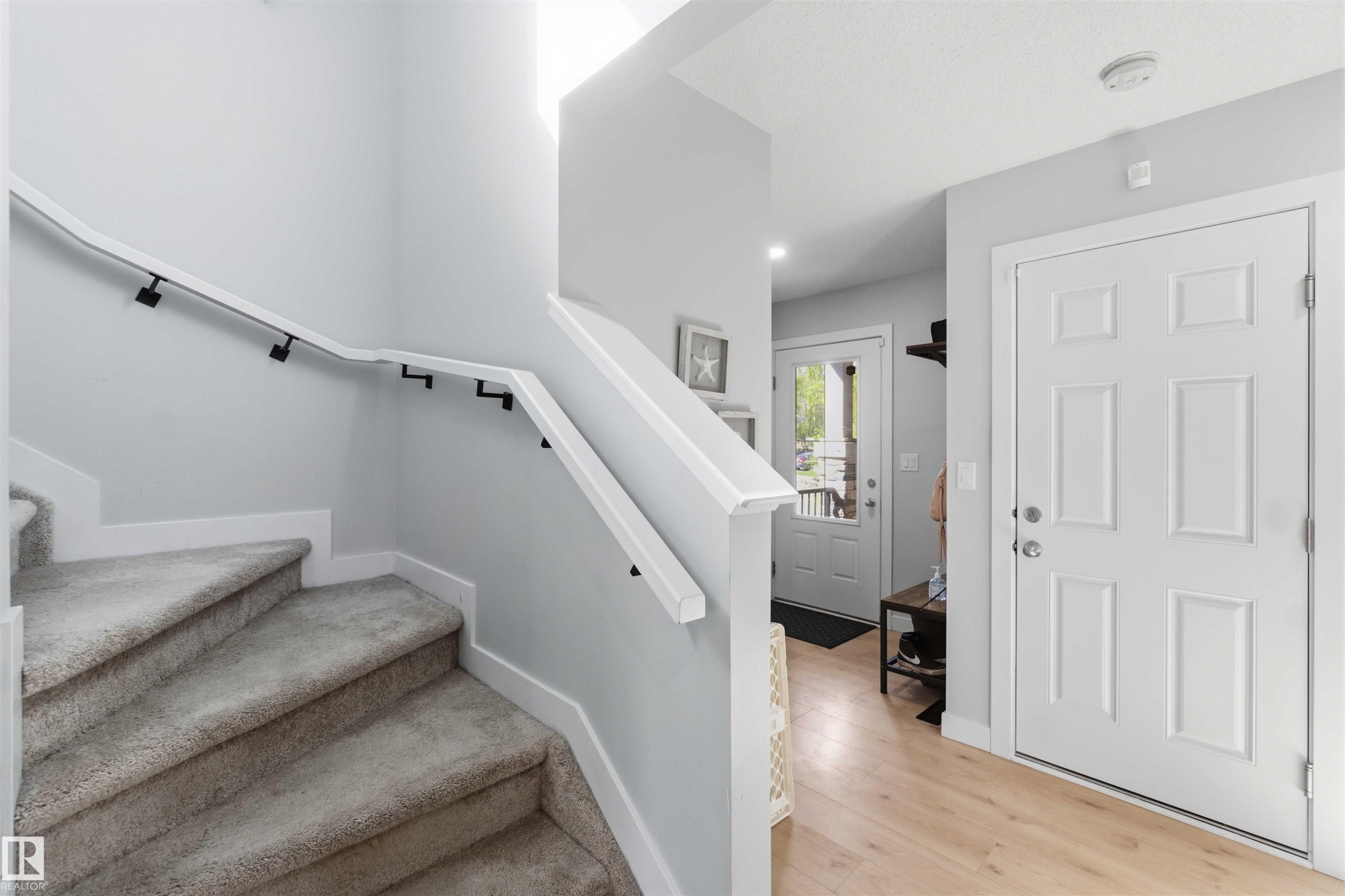 Carpeted staircase with white handrail and black supports, complemented by light wood-finish flooring - 5129 Lark Crescent, Edmonton, AB - Indoor Photo Showing Other Room