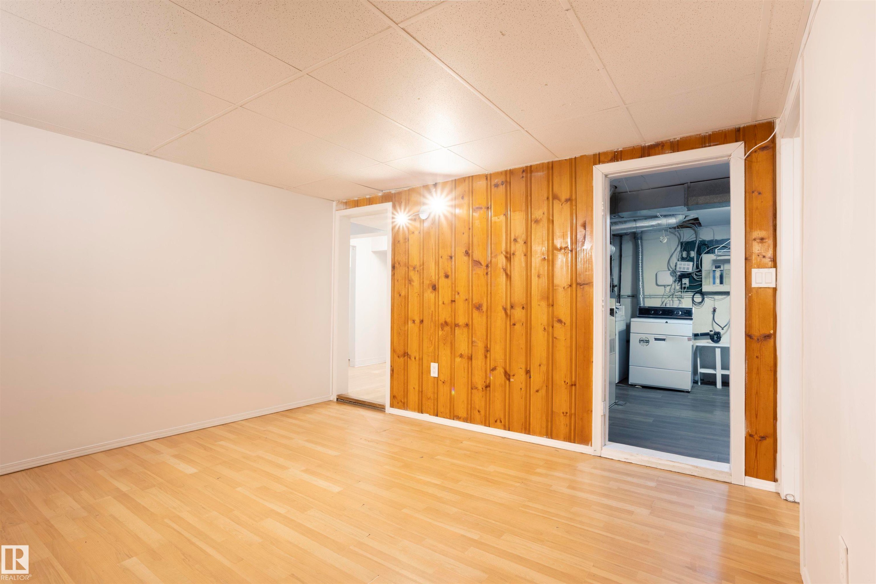Room featuring wood-finish flooring, white painted walls, and one wall with vertical wood paneling - 13716 115 Avenue, Edmonton, AB - Indoor Photo Showing Other Room