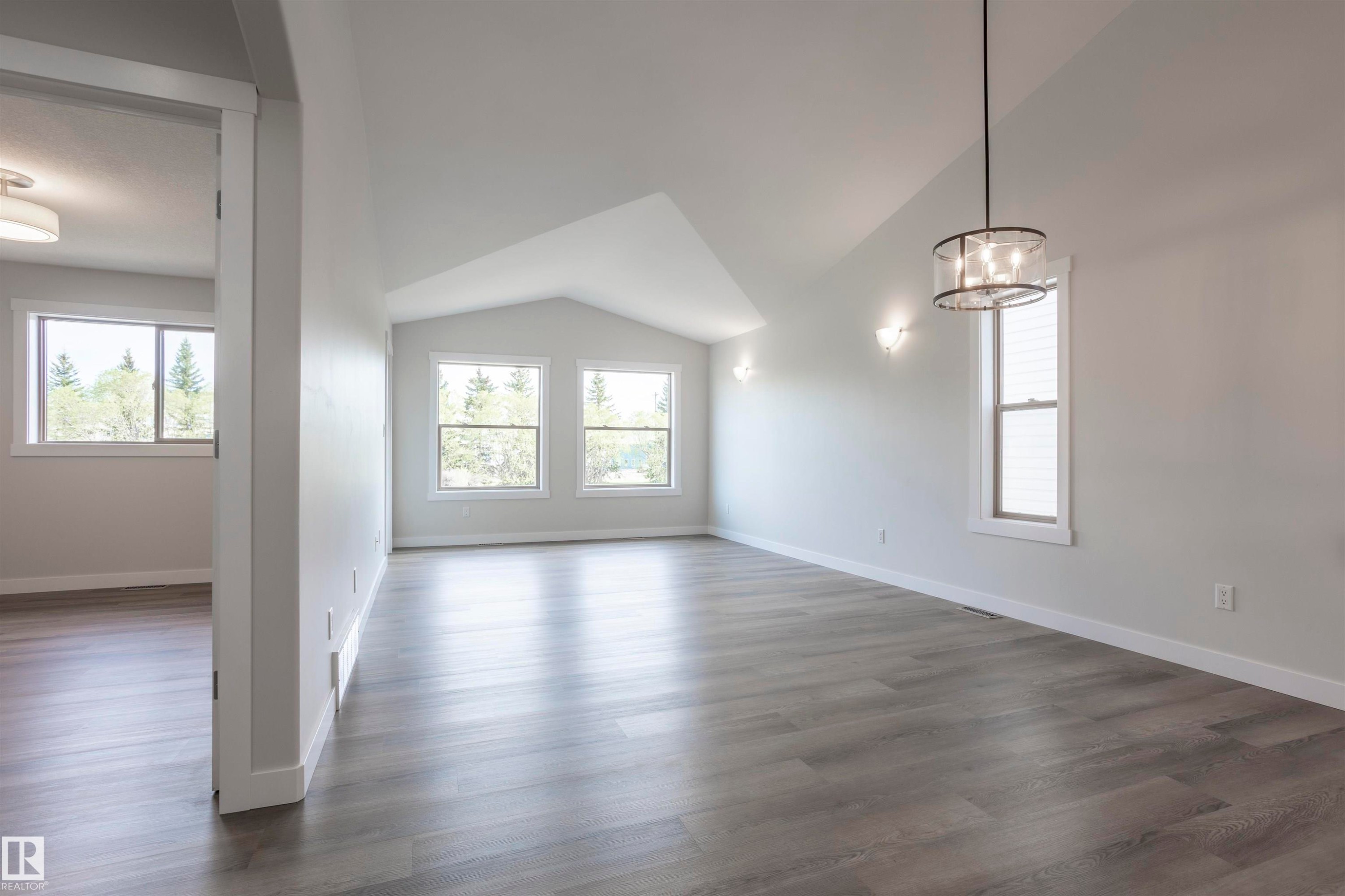 Spacious room featuring vaulted ceilings, light wood-finish flooring, multiple windows, a contemporary chandelier, and sconce lighting - 738 Kananaskis Drive, Devon, AB - Indoor Photo Showing Other Room