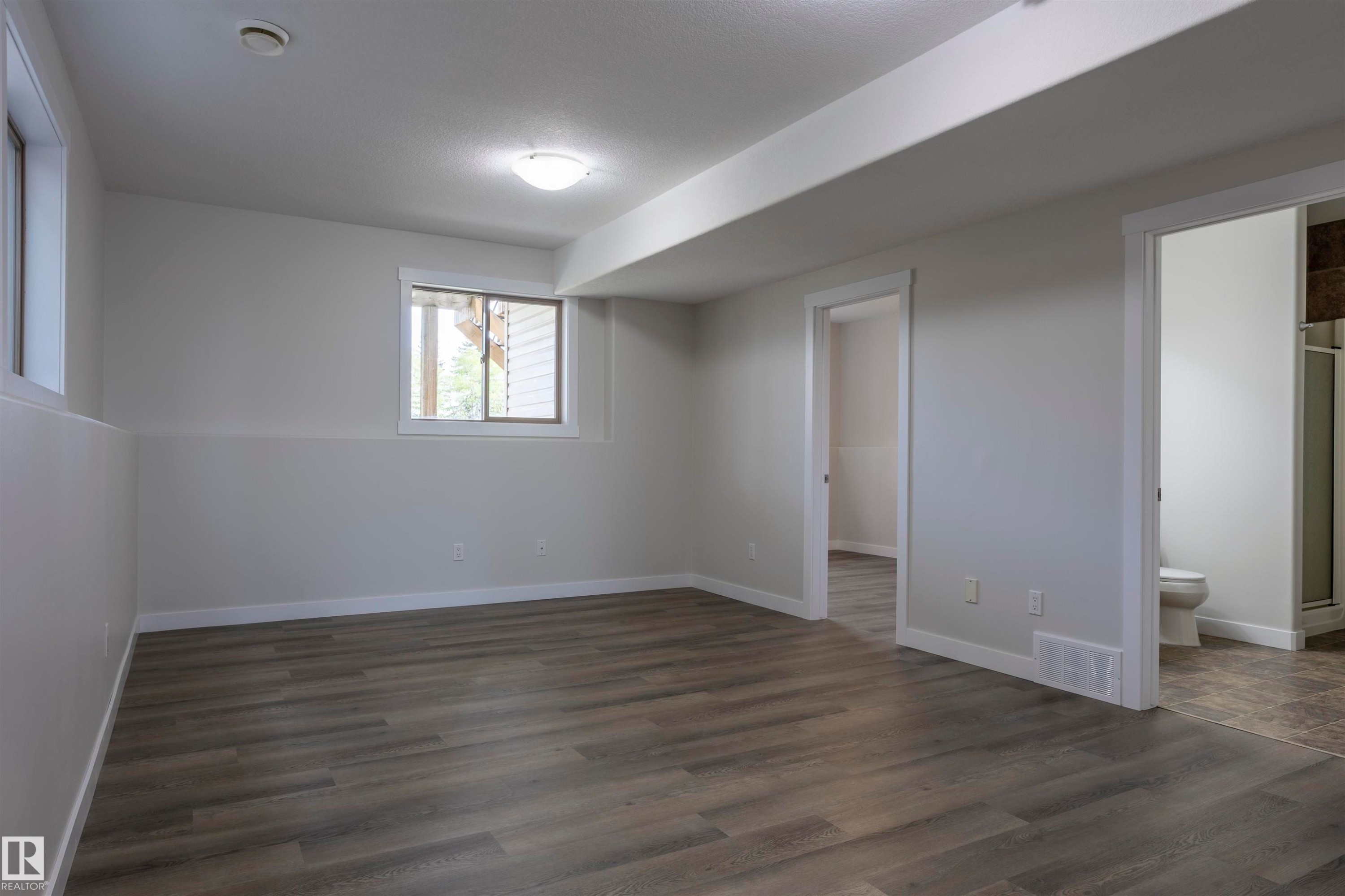 Spacious room featuring wood-finish flooring, light grey painted walls, white trim, and two windows providing natural light - 738 Kananaskis Drive, Devon, AB - Indoor Photo Showing Other Room