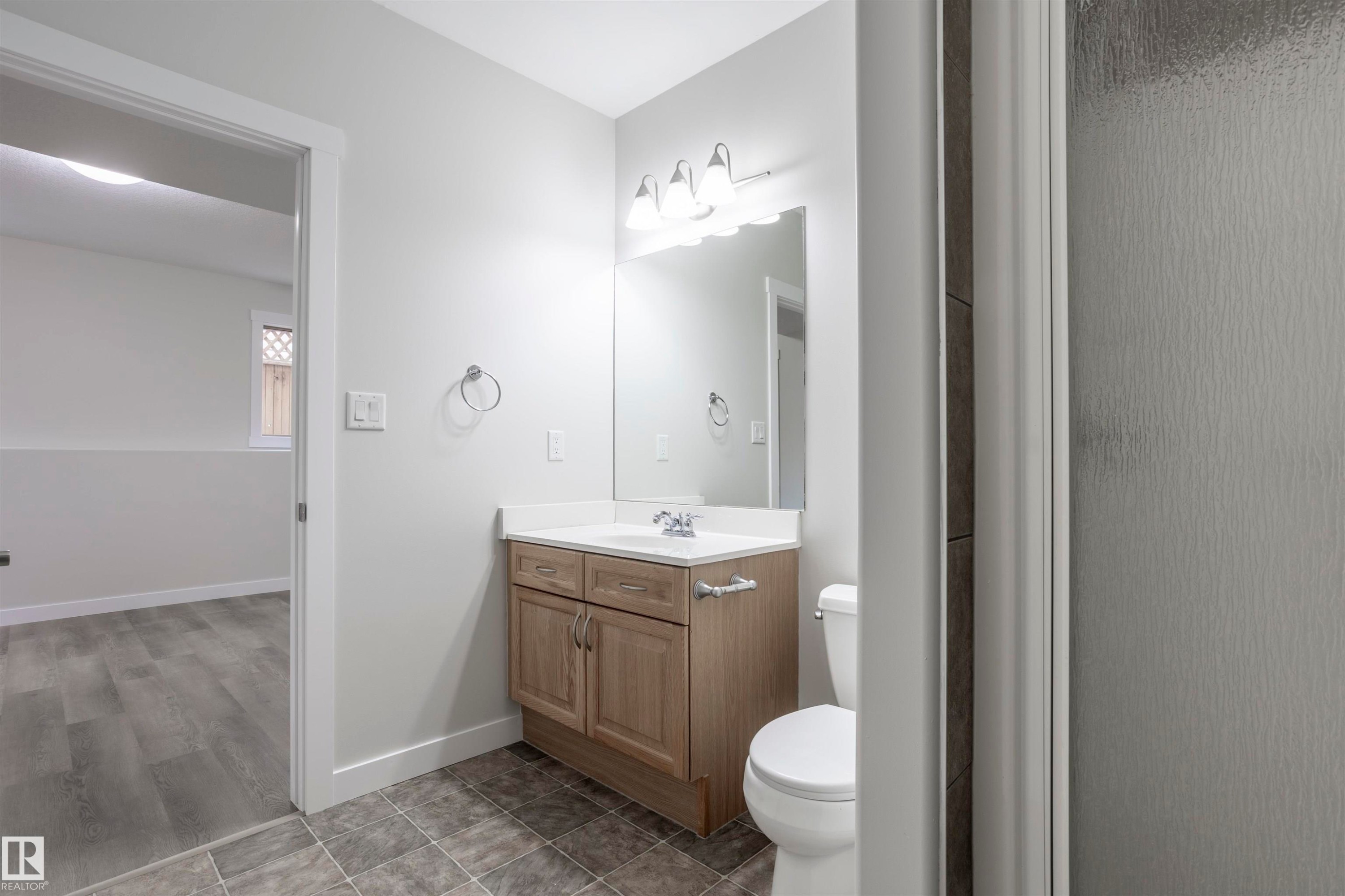 Bathroom featuring a wood-finish vanity with a white countertop, an undermount sink, and a toilet - 738 Kananaskis Drive, Devon, AB - Indoor Photo Showing Bathroom