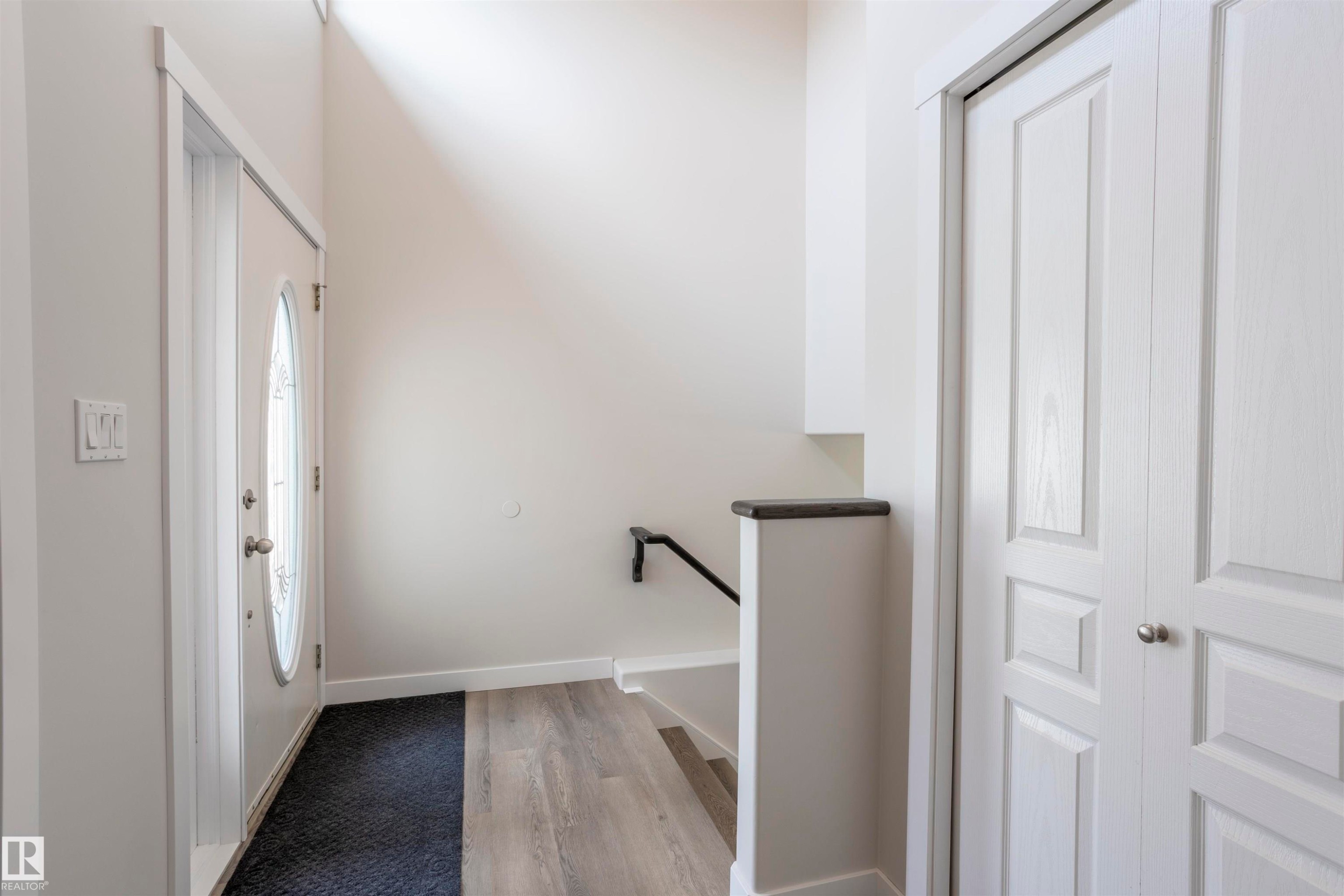 Entryway featuring a decorative glass oval insert door, wood-finish flooring, and a white paneled closet - 738 Kananaskis Drive, Devon, AB - Indoor Photo Showing Other Room
