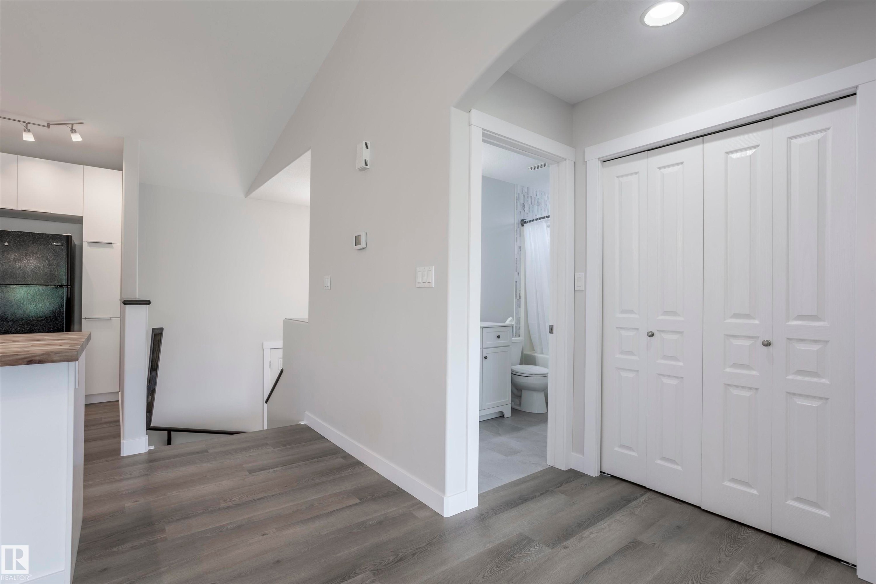Entryway with wood-finish flooring, white bi-fold closet doors, recessed lighting, and an archway leading to a bathroom featuring a white vanity and toilet - 738 Kananaskis Drive, Devon, AB - Indoor