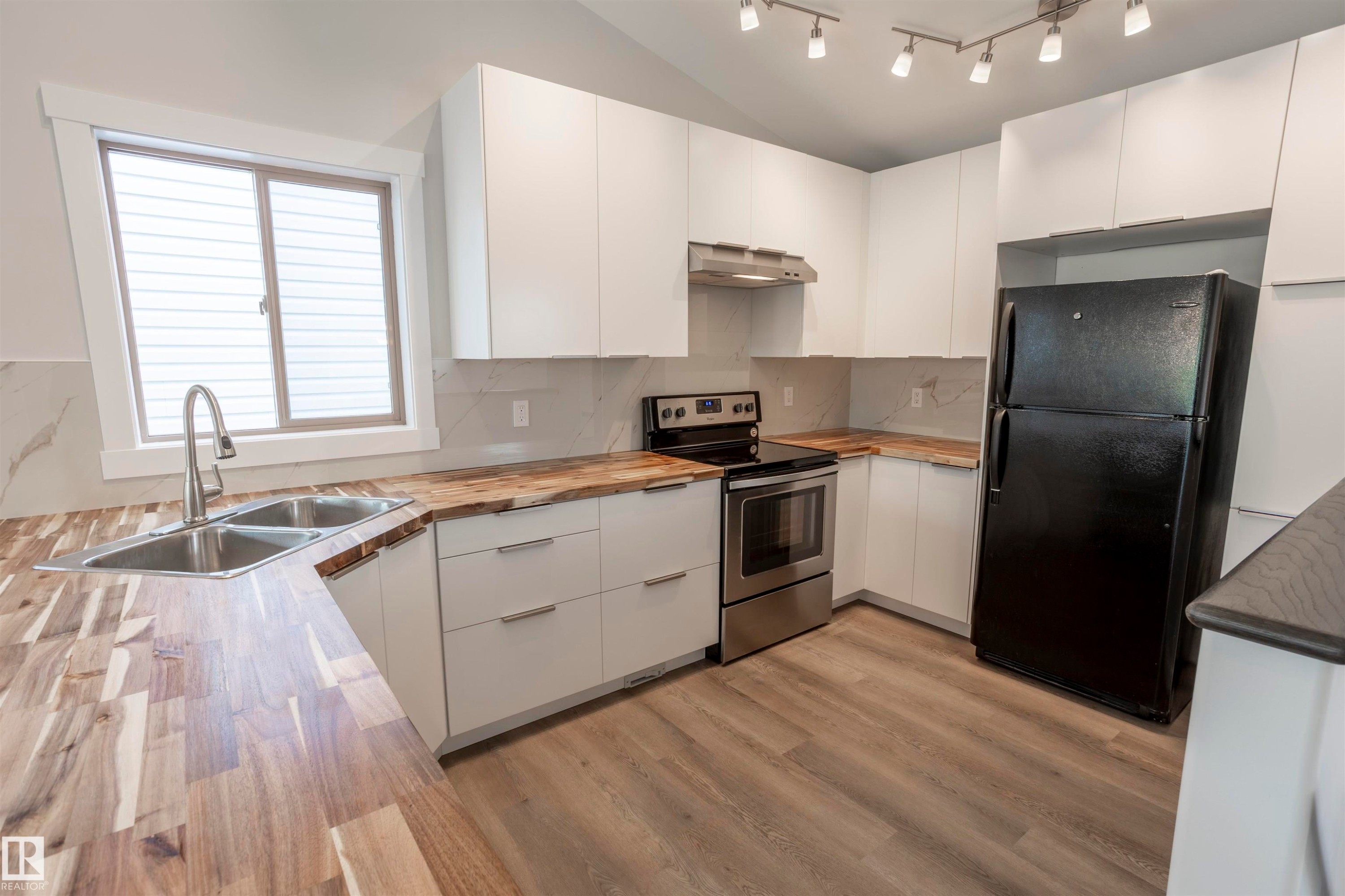 Modern kitchen featuring butcher block countertops, white flat-panel cabinetry, a stainless steel oven/range, and a dual basin sink with a gooseneck faucet - 738 Kananaskis Drive, Devon, AB - Indoor Photo Showing Kitchen With Double Sink