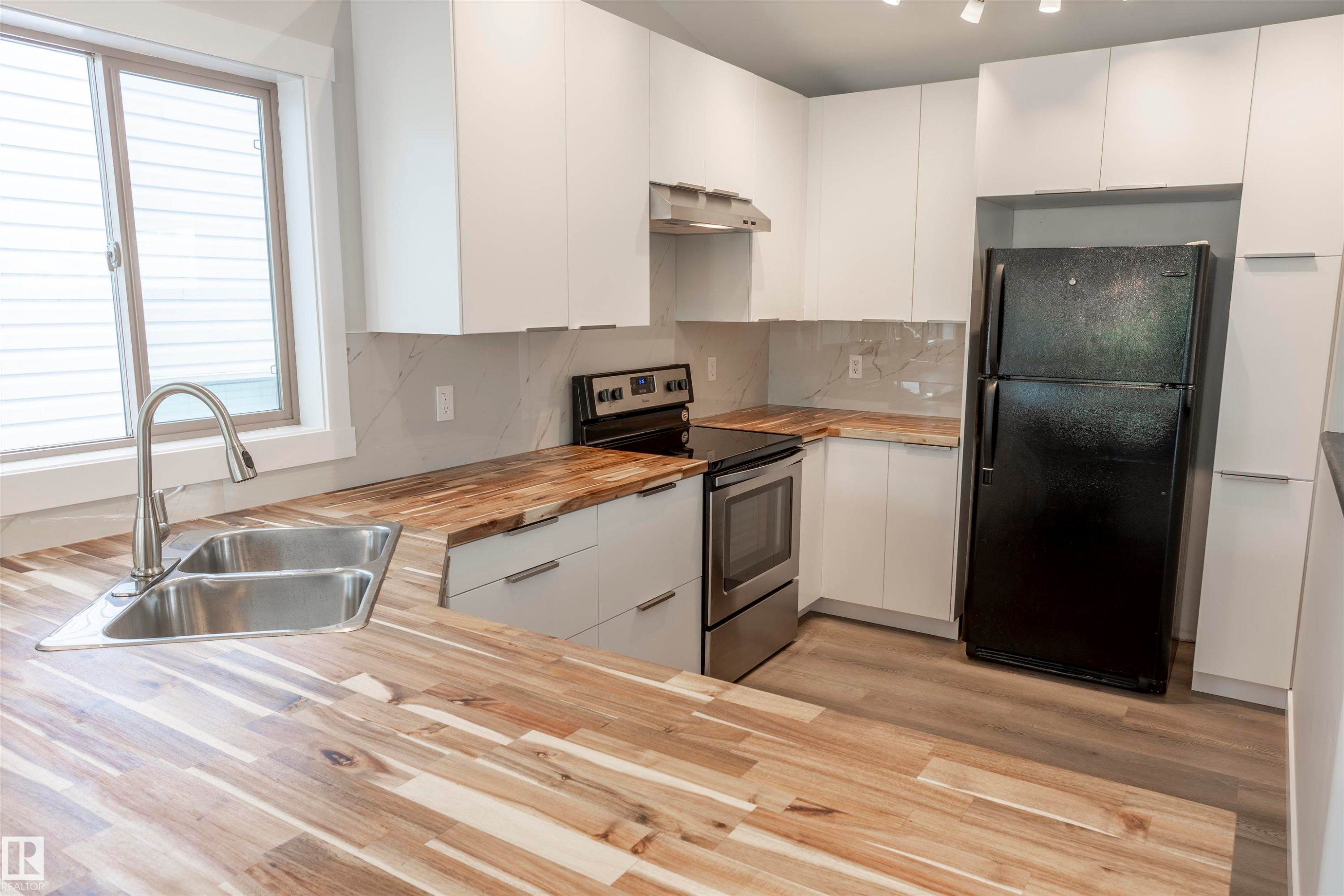 Kitchen featuring butcher block countertops, white flat-panel cabinetry, stainless steel sink with pull-down faucet, and light wood-finish flooring - 738 Kananaskis Drive, Devon, AB - Indoor Photo Showing Kitchen With Double Sink