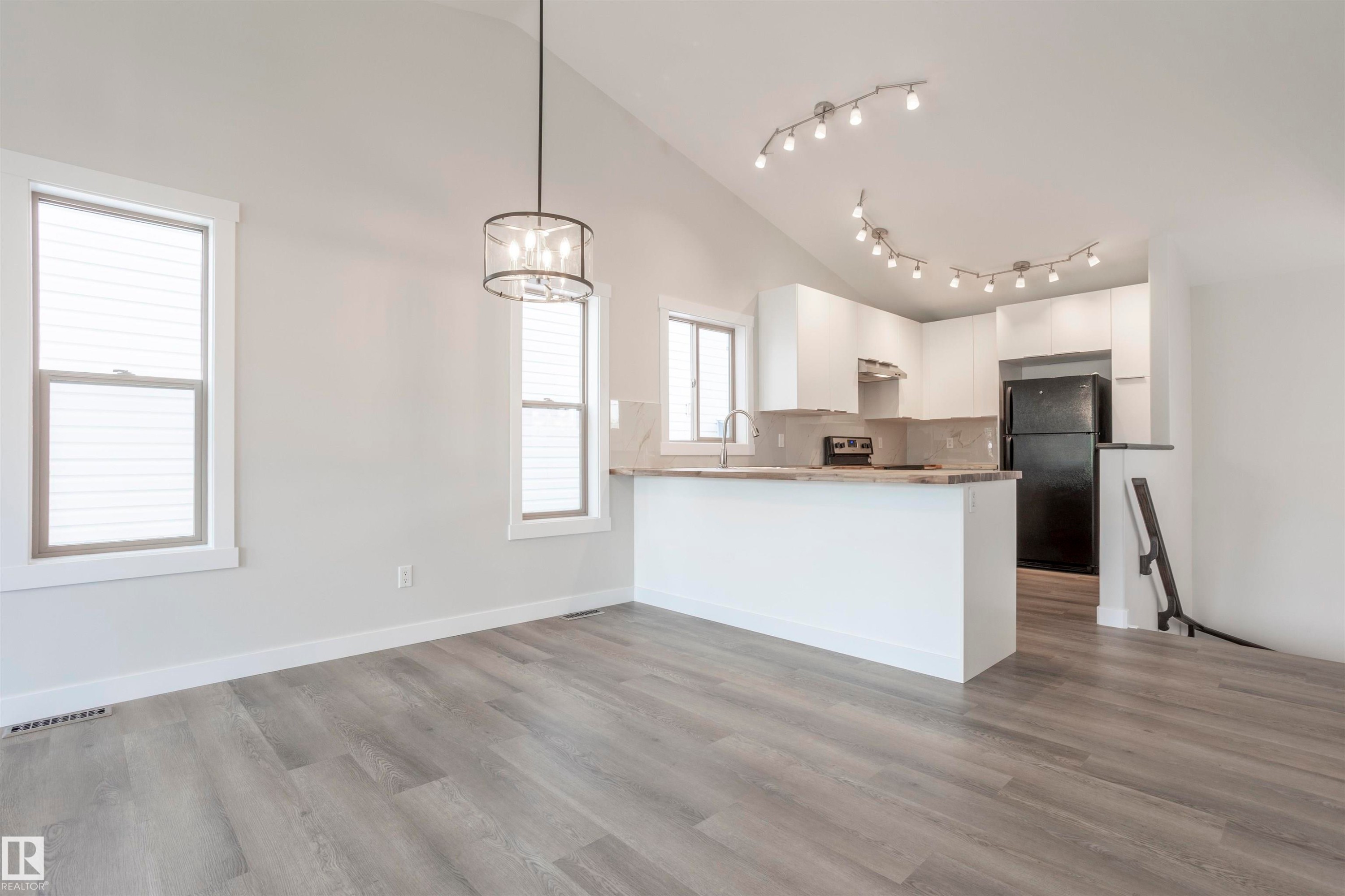 Vaulted ceilings with contemporary lighting fixtures, light wood-finish flooring, and a kitchen featuring white cabinetry, a light-toned countertop, and a tile backsplash - 738 Kananaskis Drive, Devon, AB - Indoor Photo Showing Kitchen