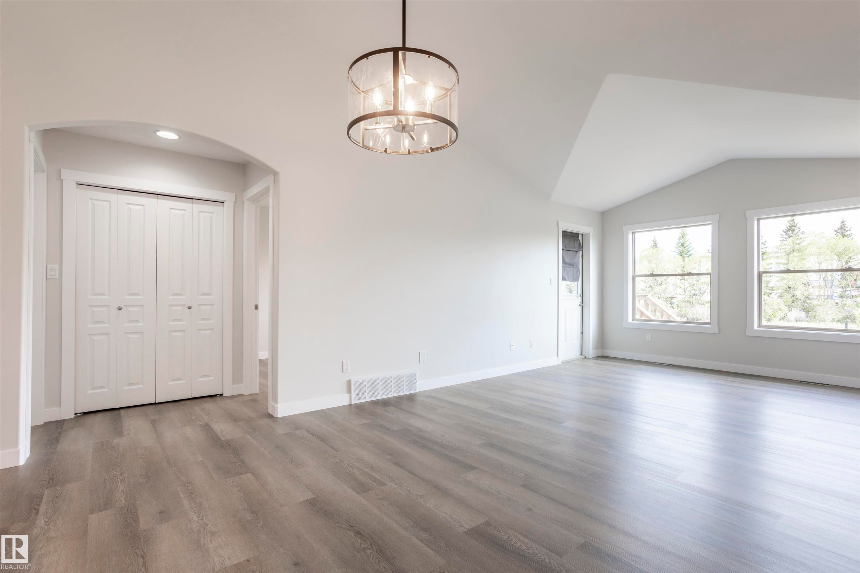 Spacious interior featuring wood-finish flooring, vaulted ceilings, and a modern drum chandelier - 738 Kananaskis Drive, Devon, AB - Indoor Photo Showing Other Room