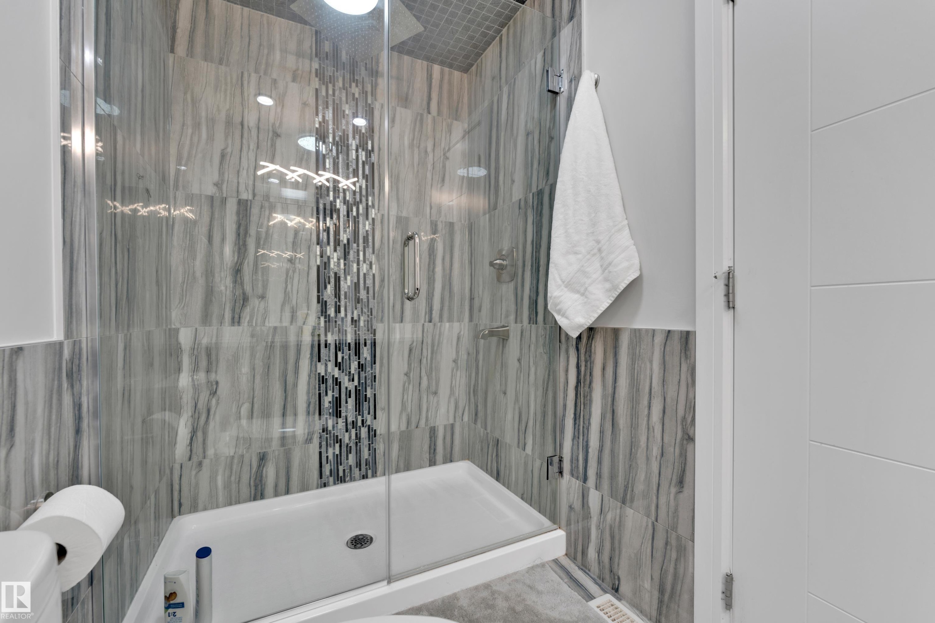 Walk-in shower featuring glass enclosure, gray veined tile walls, and a mosaic tile accent strip - 9329 Connors Road, Edmonton, AB - Indoor Photo Showing Bathroom
