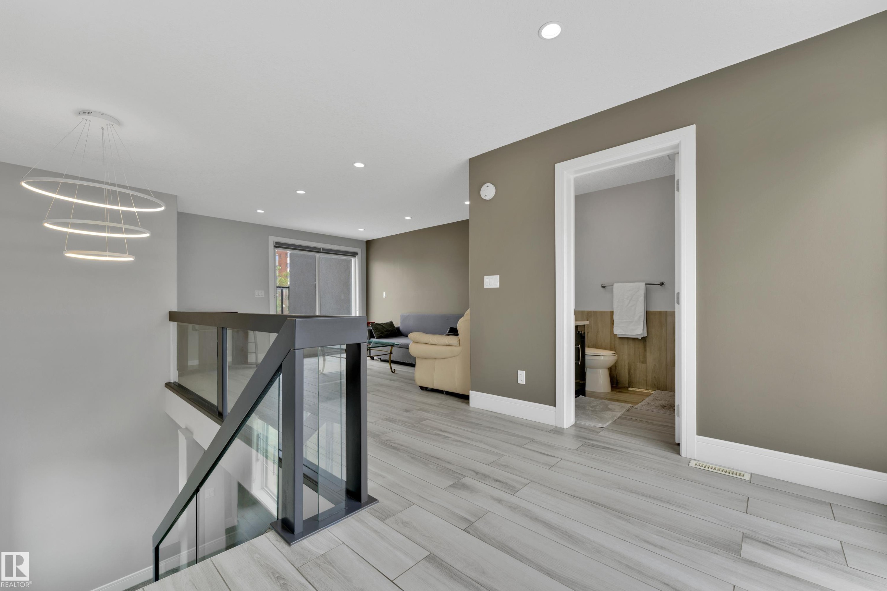 Modern open-concept upper level featuring sleek glass and metal railings, contemporary circular pendant lighting, wood-finish flooring, recessed ceiling lights, and a convenient powder room - 9329 Connors Road, Edmonton, AB - Indoor Photo Showing Other Room