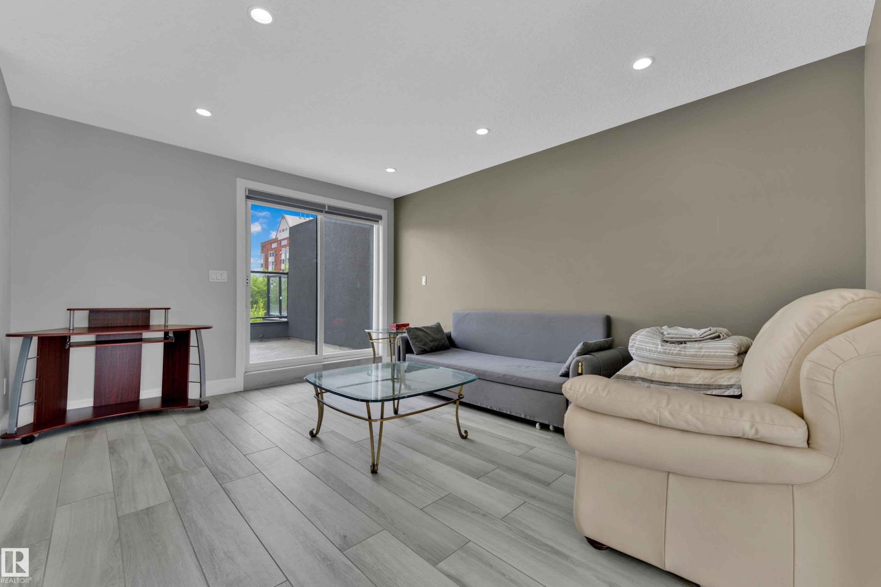 Spacious living area featuring light wood-finish flooring, recessed lighting, and a sliding glass door providing access to an outdoor balcony - 9329 Connors Road, Edmonton, AB - Indoor