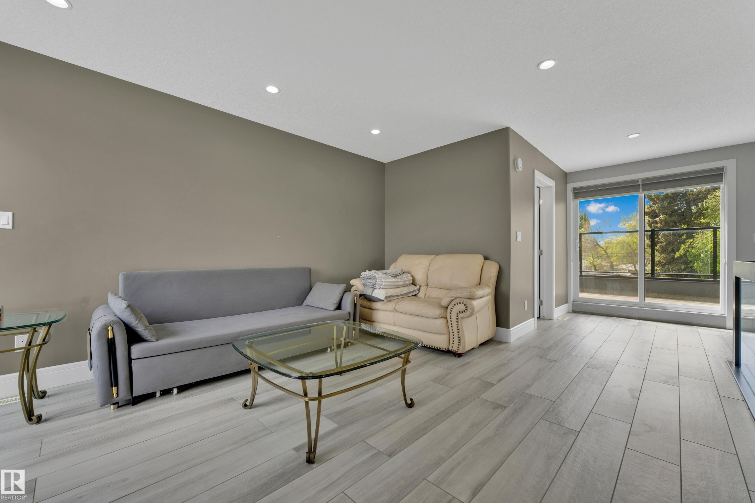 Spacious living area featuring light wood-finish flooring, recessed lighting, and direct patio access through a large sliding glass door - 9329 Connors Road, Edmonton, AB - Indoor