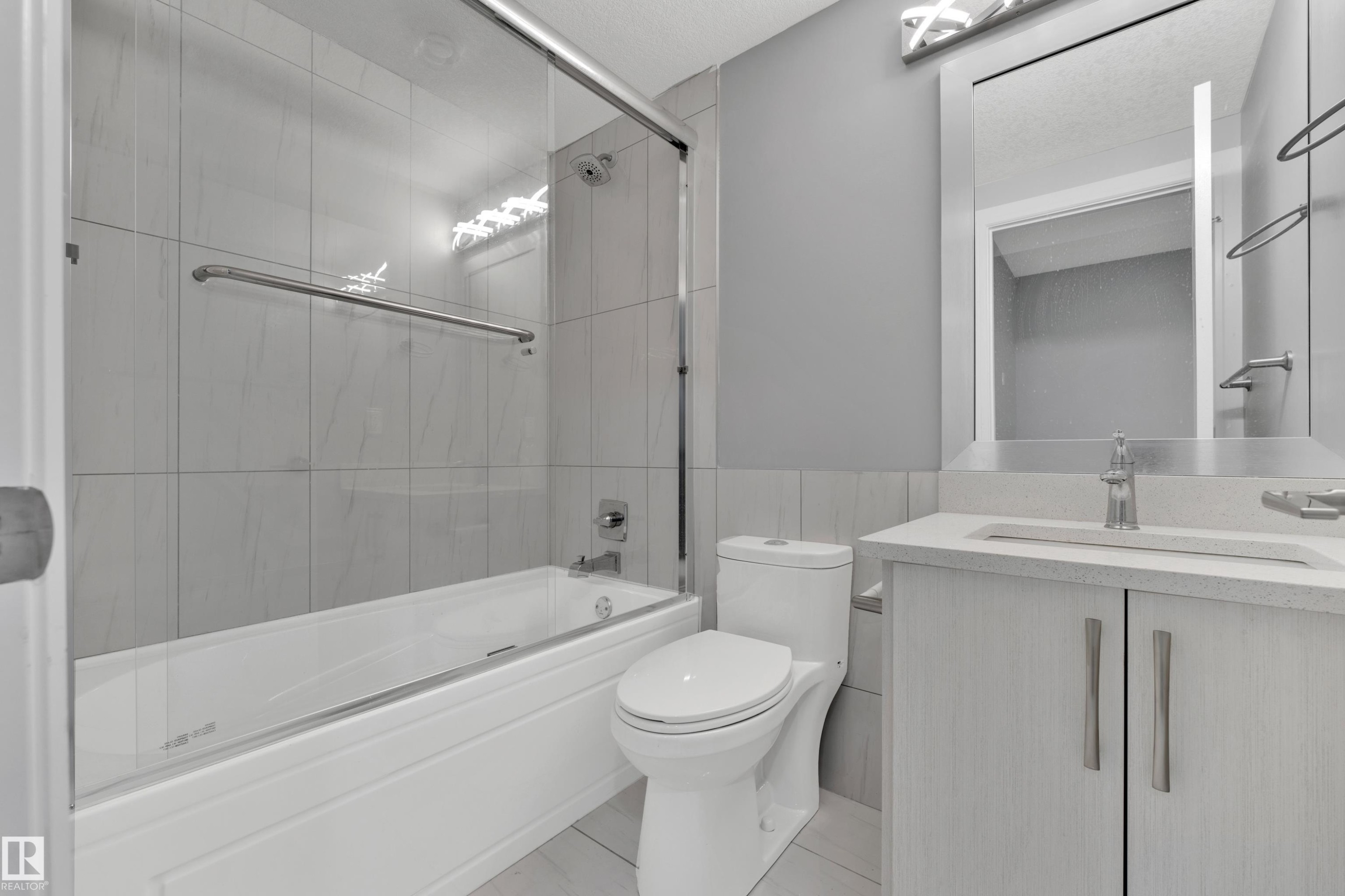 Bathroom featuring a tub and shower combination with glass enclosure, white tile surround, and a coordinating vanity with a light countertop and undermount sink - 9329 Connors Road, Edmonton, AB - Indoor Photo Showing Bathroom