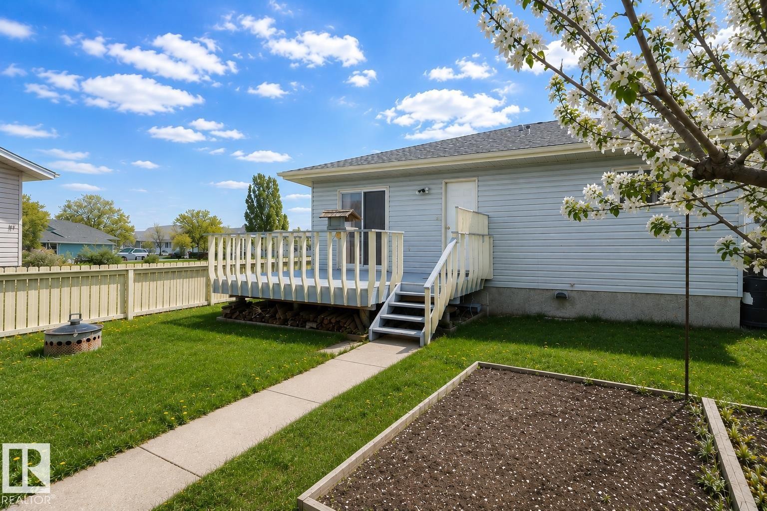 Expansive rear yard featuring a raised wood deck with steps, a concrete walkway, a defined garden bed, and a fenced perimeter - 4005 55 Avenue, Whitecourt, AB - Outdoor