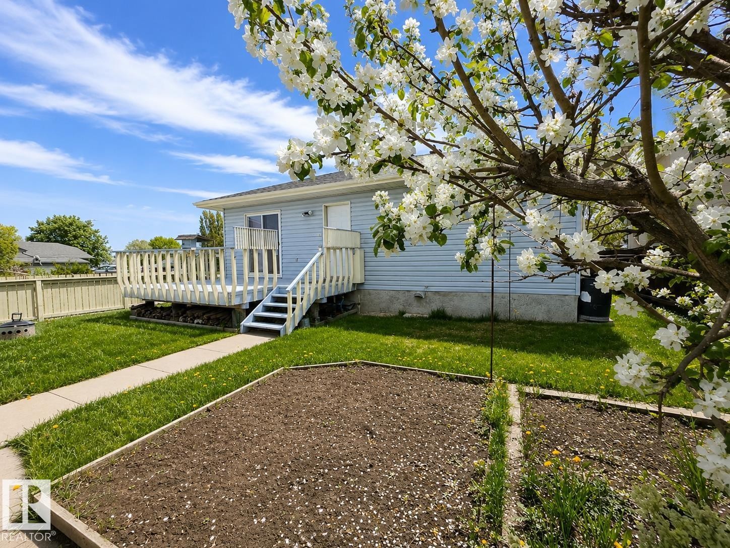 Rear exterior featuring light blue siding and a spacious wooden deck with railings - 4005 55 Avenue, Whitecourt, AB - Outdoor