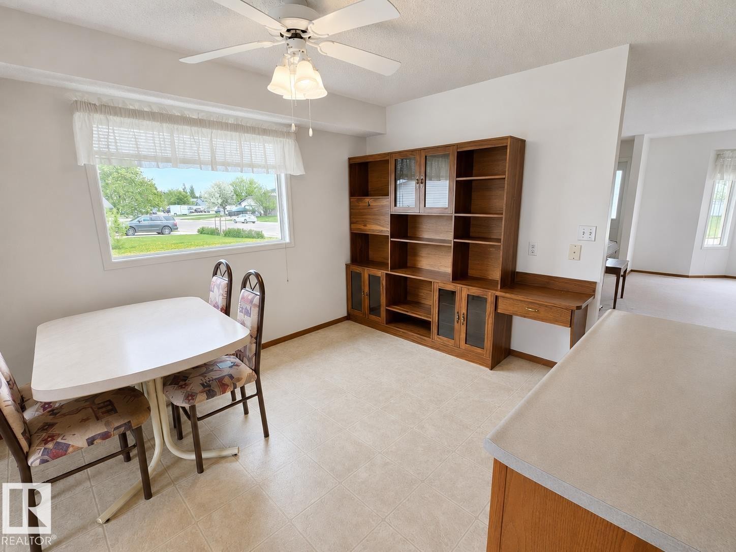Dining area featuring neutral tile flooring and a built-in wood-finish storage unit with glass-front cabinets and an integrated desk - 4005 55 Avenue, Whitecourt, AB - Indoor