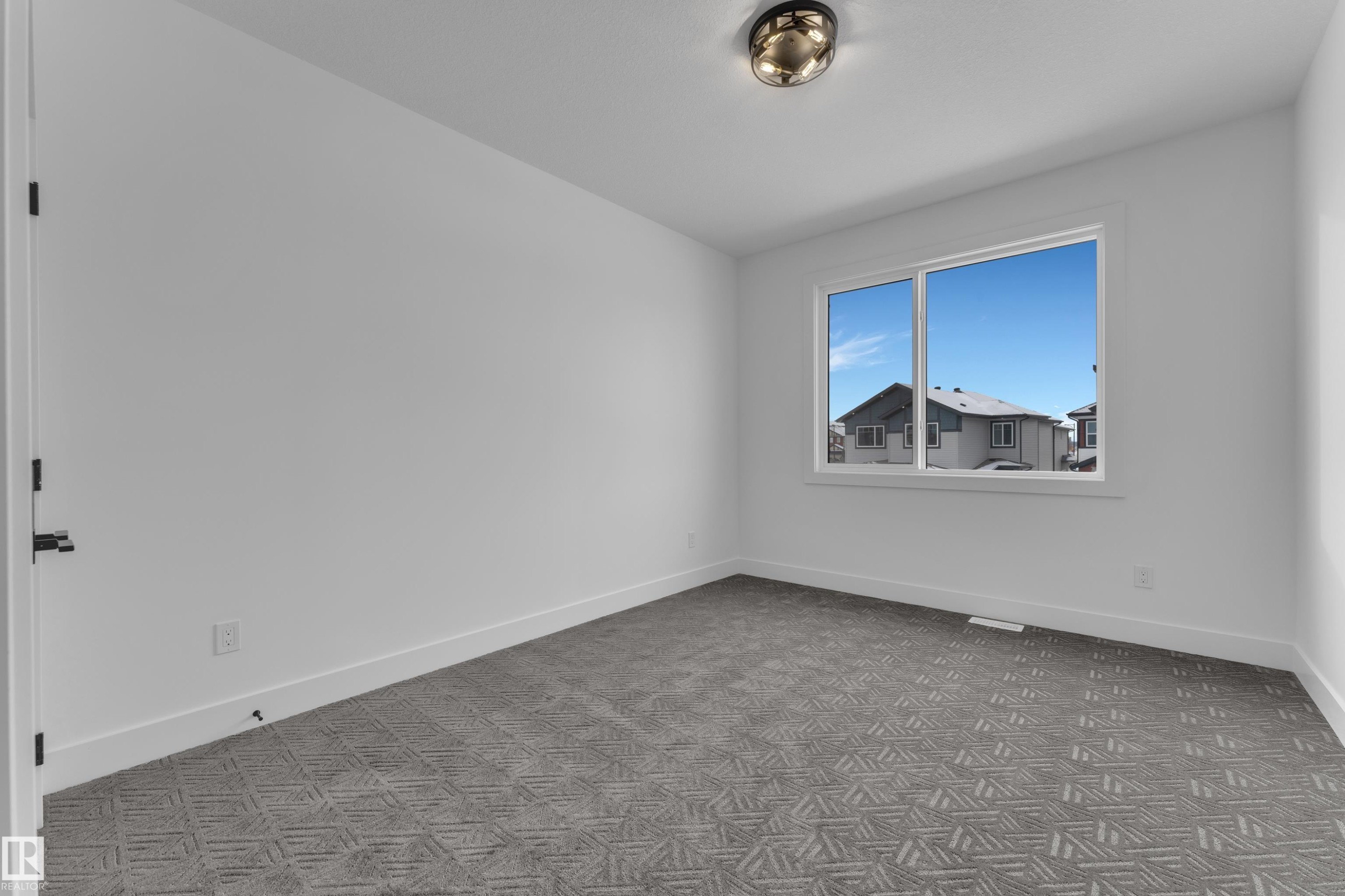 Bright room featuring a large window, patterned carpet flooring, white baseboards, and a contemporary flush-mount ceiling light fixture - 2027 156 Avenue, Edmonton, AB - Indoor Photo Showing Other Room