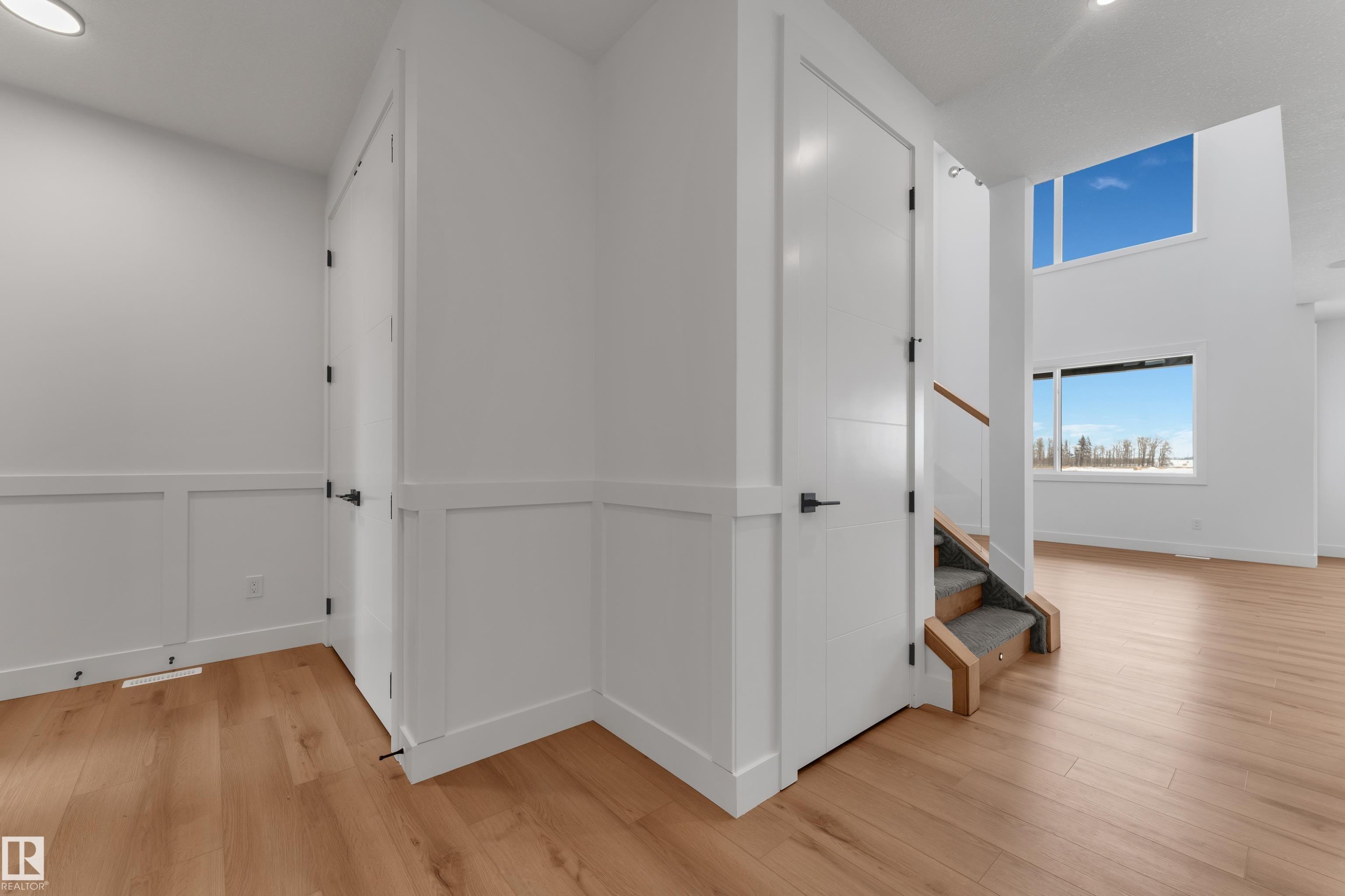Entryway featuring crisp white wainscoting, wood-finish flooring, and a staircase with wood railing and carpeted treads - 2027 156 Avenue, Edmonton, AB - Indoor Photo Showing Other Room