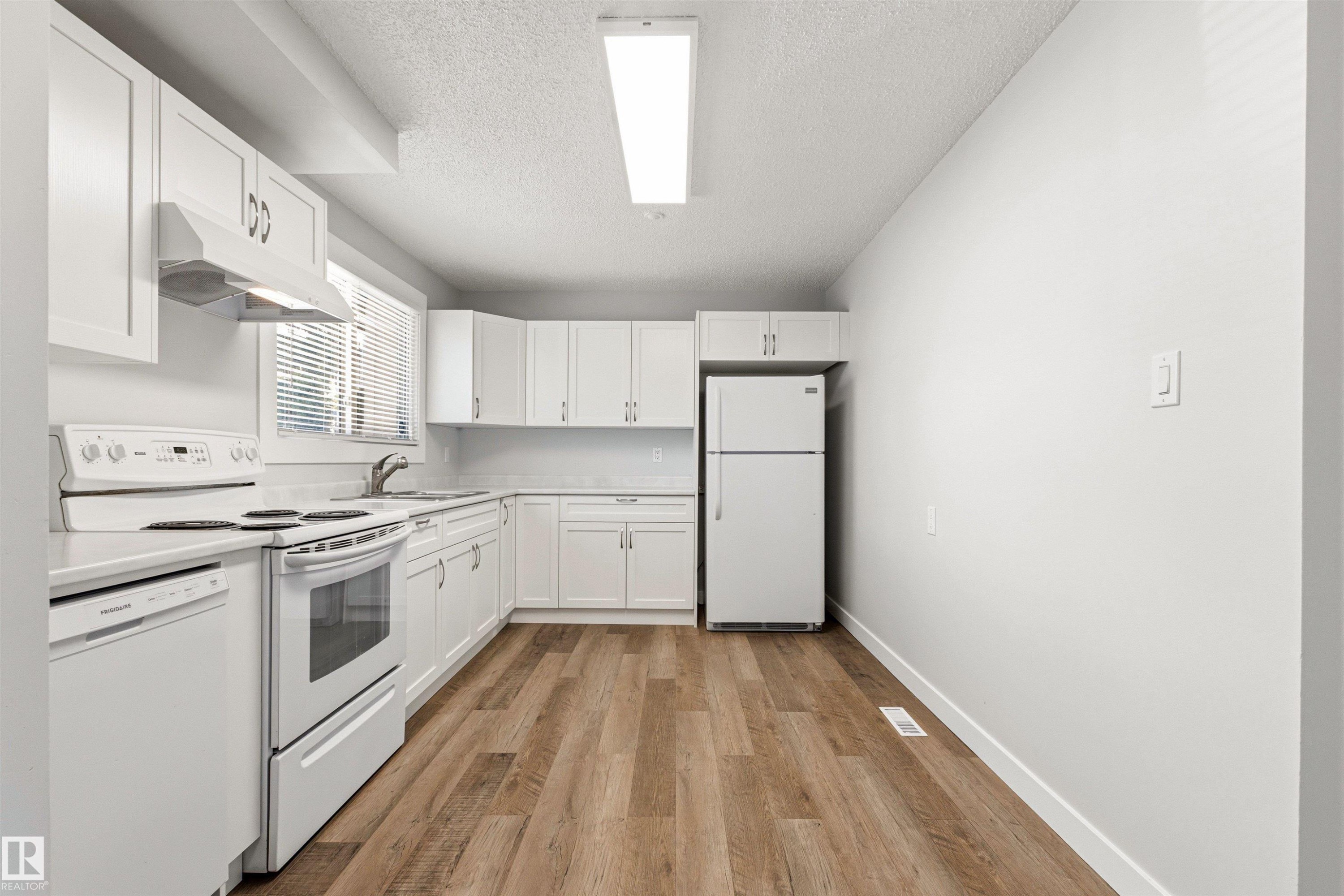 Bright kitchen featuring white cabinetry, a white appliance package, wood-finish flooring, ample counter space, and a window with blinds - 707 Clareview Road, Edmonton, AB - Indoor Photo Showing Kitchen