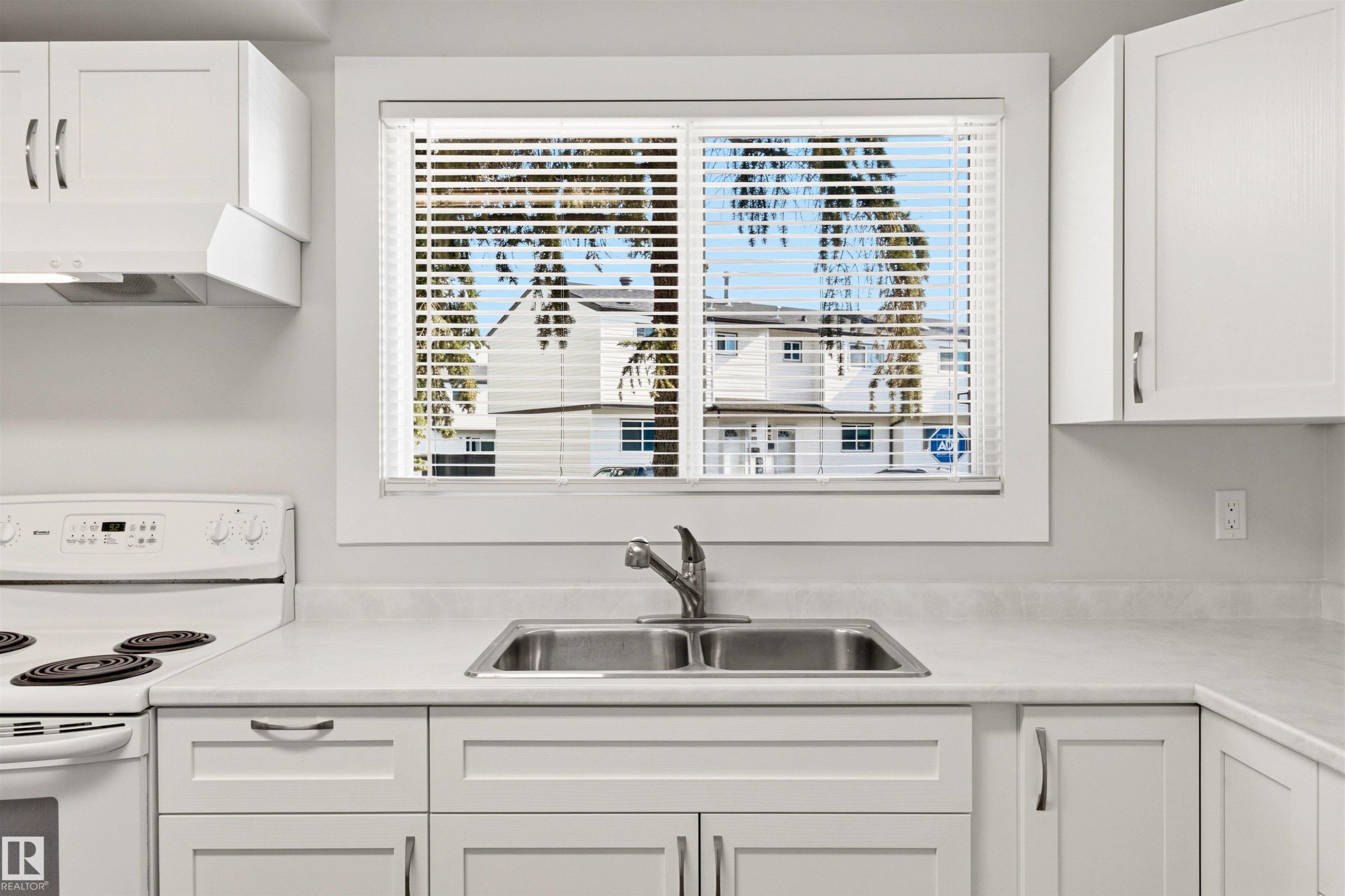 Kitchen featuring white cabinetry with brushed nickel hardware, a double basin stainless steel sink, a window with horizontal blinds, and a white electric range with an overhead range hood - 707 Clareview Road, Edmonton, AB - Indoor Photo Showing Kitchen With Double Sink