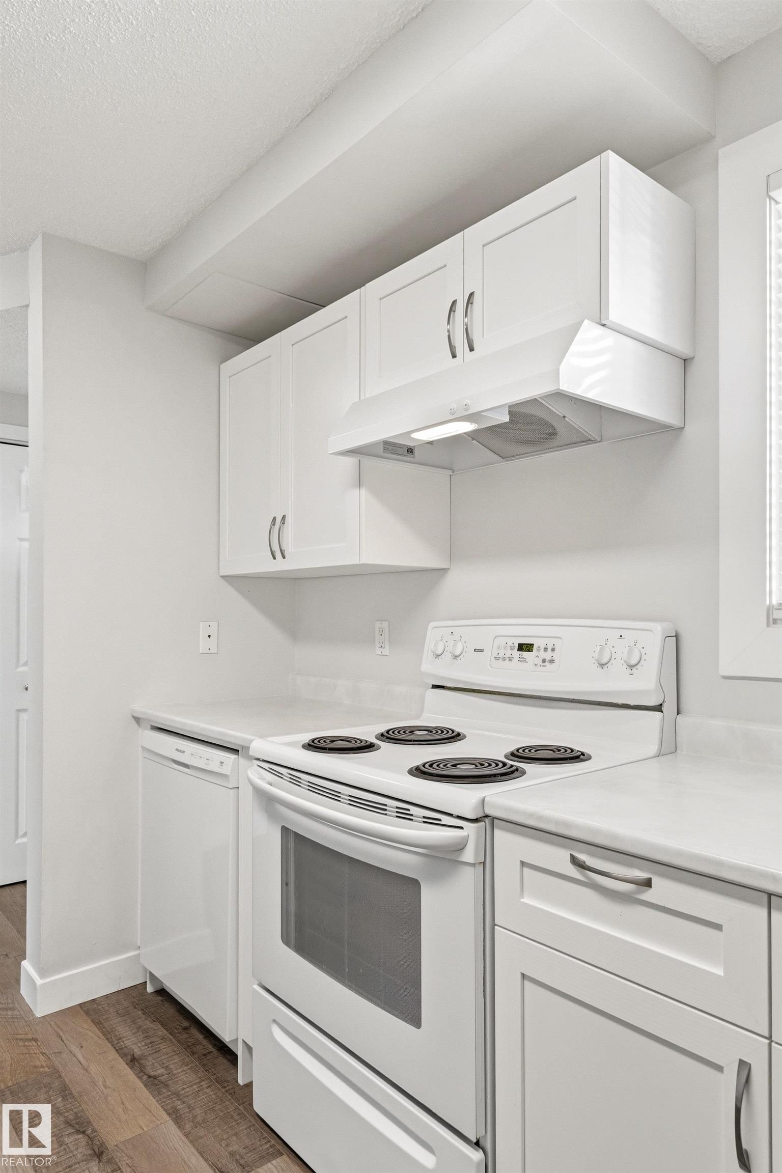 Kitchen workspace featuring white cabinetry, a built-in range, a dishwasher, and light-toned countertops - 707 Clareview Road, Edmonton, AB - Indoor Photo Showing Kitchen