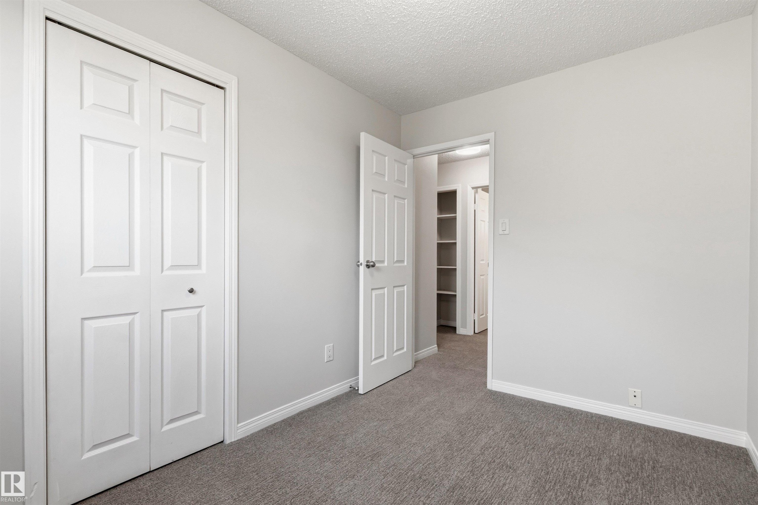 Neutral-toned room featuring a bifold closet door, a paneled interior door, and grey carpeting - 707 Clareview Road, Edmonton, AB - Indoor Photo Showing Other Room