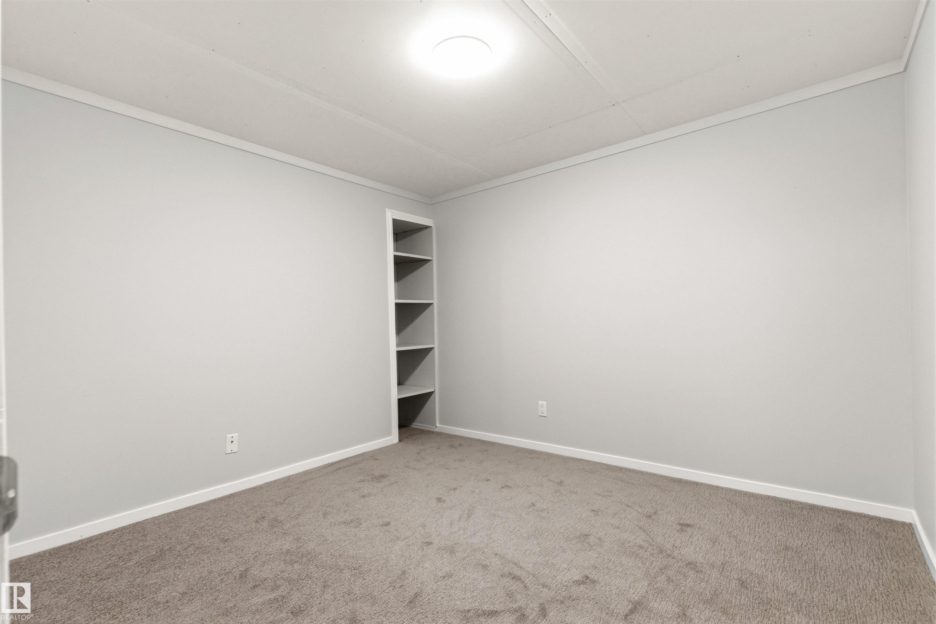 Spacious room featuring light gray walls, plush gray carpeting, white baseboards, and a built-in corner shelving unit - 707 Clareview Road, Edmonton, AB - Indoor Photo Showing Other Room