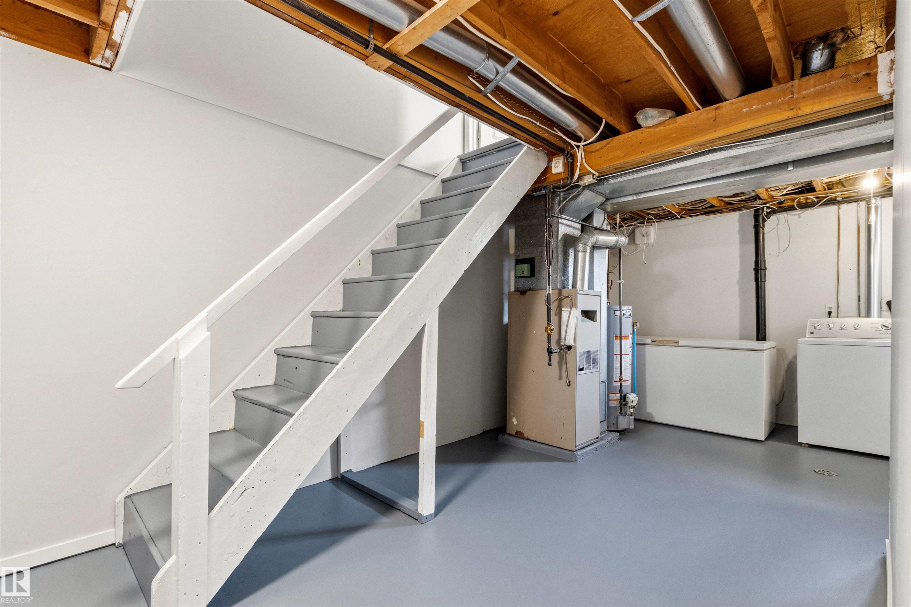 Basement area featuring a painted wooden staircase with handrail, exposed wood ceiling joists, and a light gray finished floor - 707 Clareview Road, Edmonton, AB - Indoor Photo Showing Laundry Room