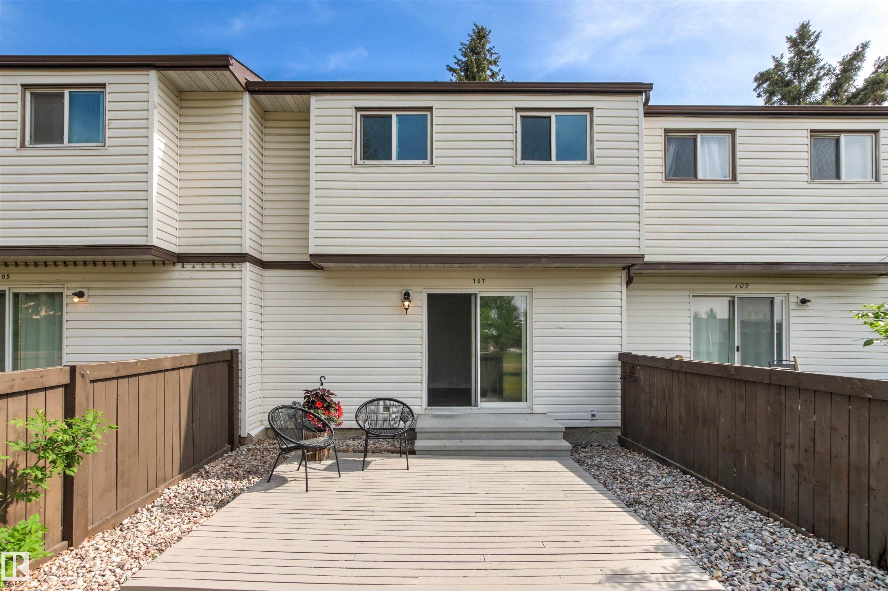 Private patio area featuring a light-toned decking surface, surrounded by a wood fence and gravel landscaping - 707 Clareview Road, Edmonton, AB - Outdoor With Exterior