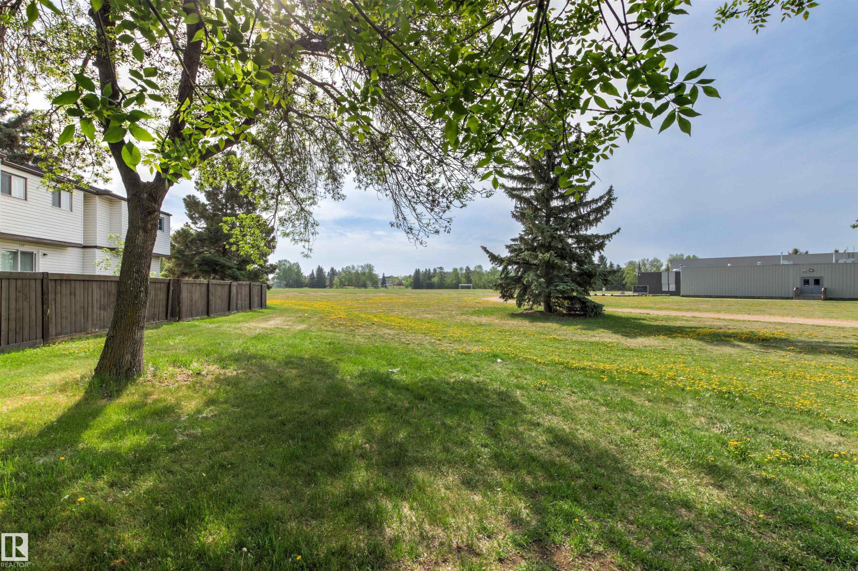 Expansive green space featuring a large field, mature trees, and a wooden privacy fence - 707 Clareview Road, Edmonton, AB - Outdoor