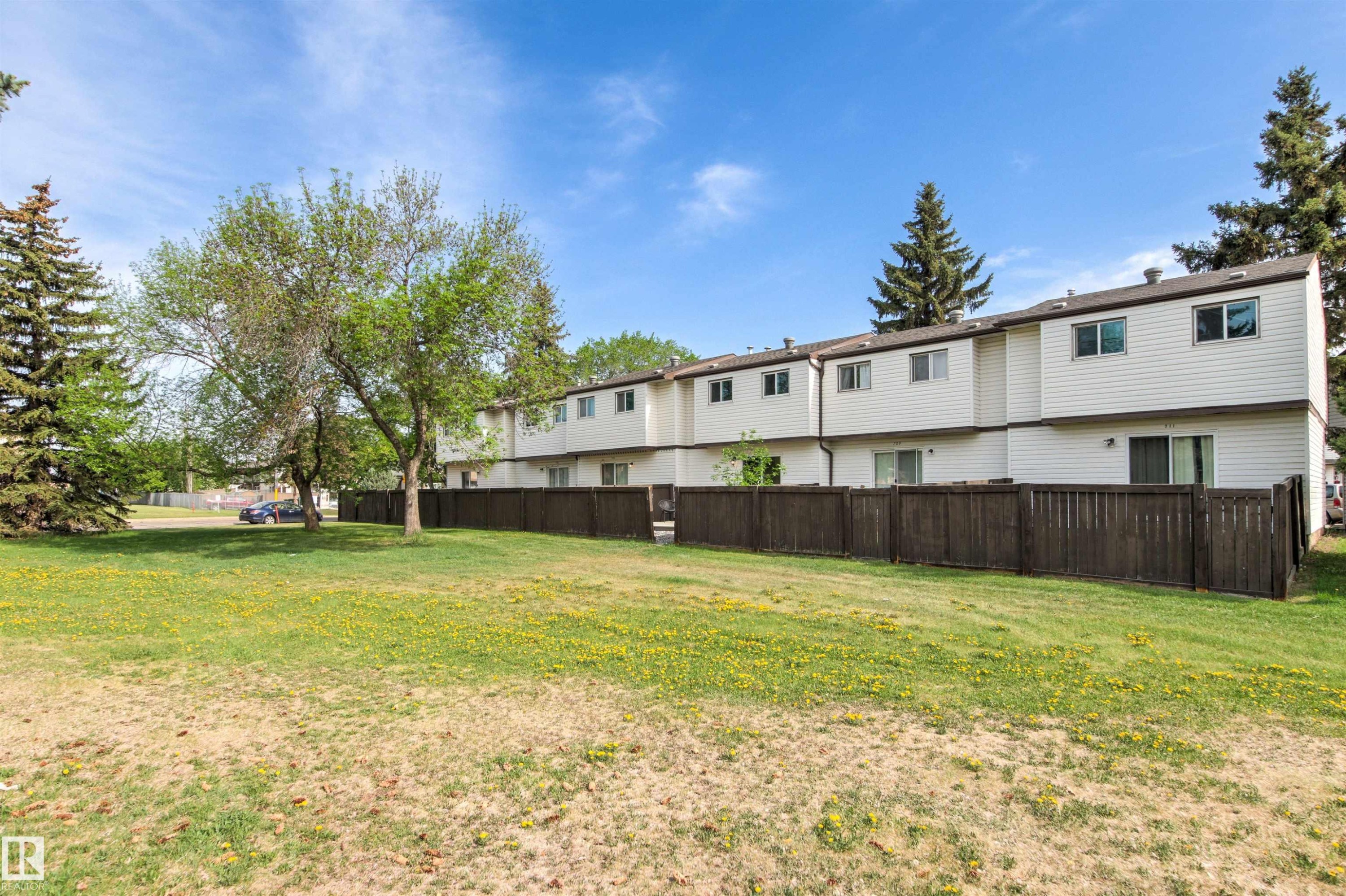 Rear exterior of a multi-unit property featuring white siding and dark brown fencing - 707 Clareview Road, Edmonton, AB - Outdoor