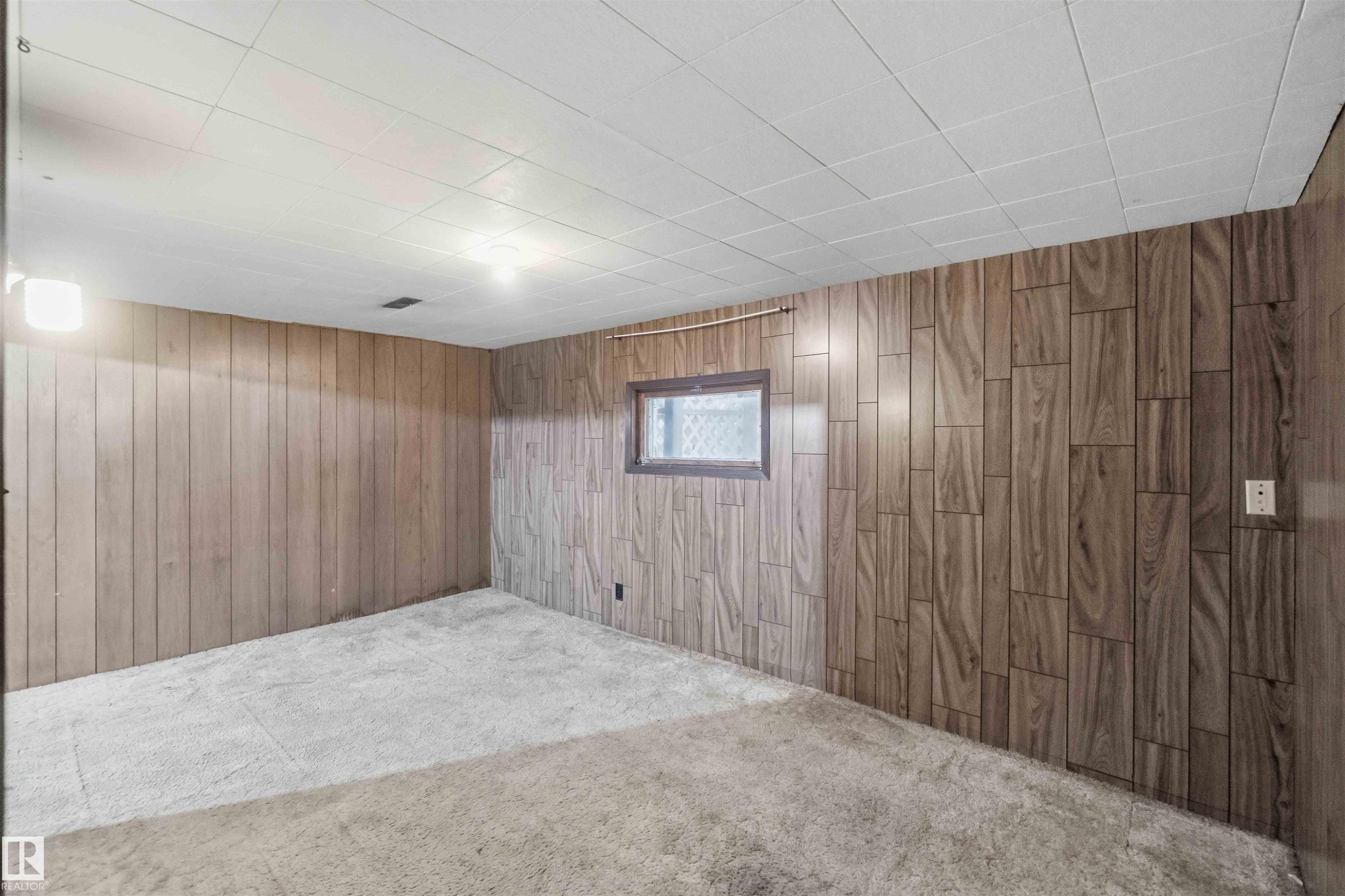 Carpeted room featuring wood-finish paneling and a drop ceiling - 16 Michigan Street, Devon, AB - Indoor