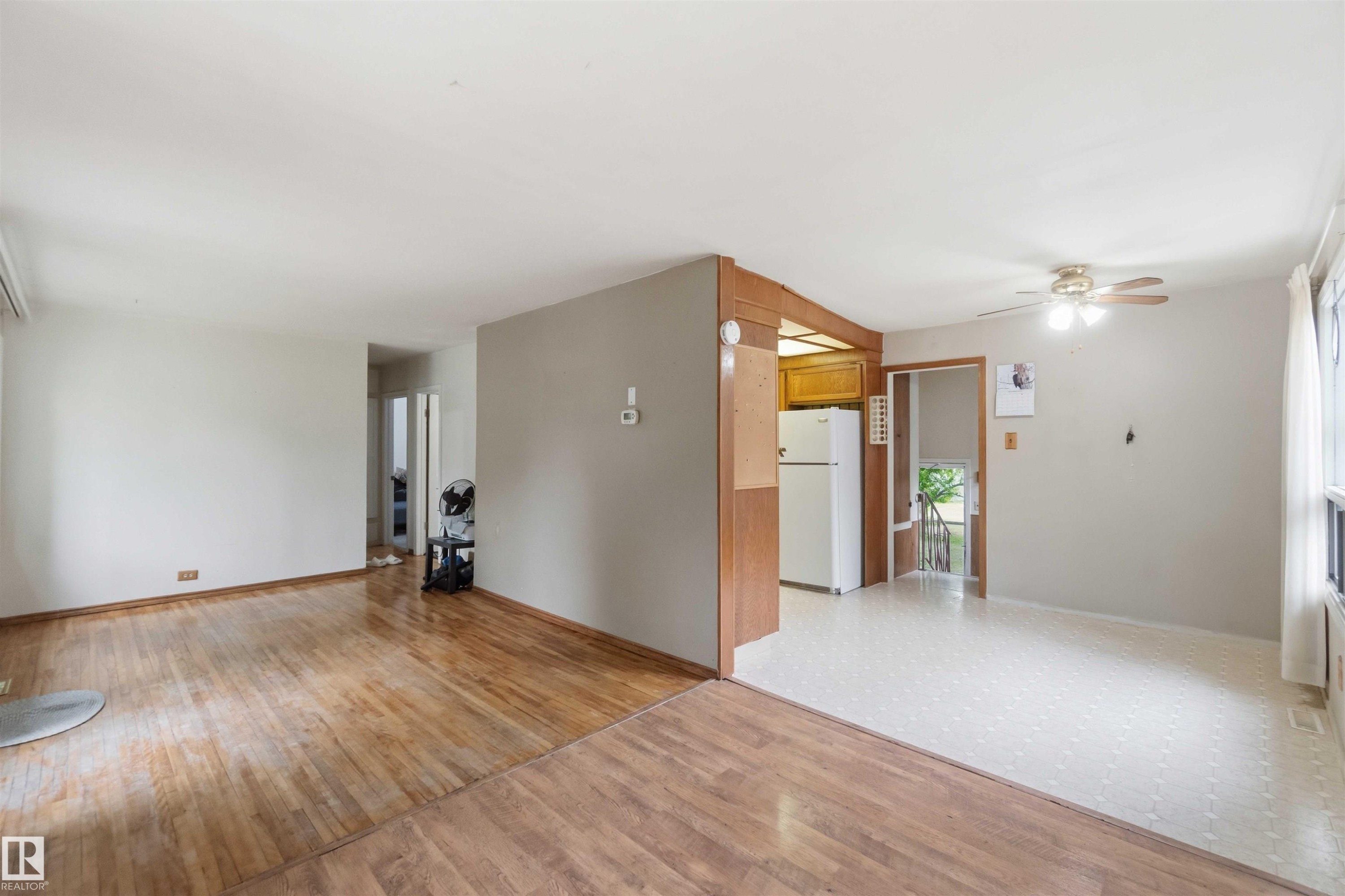 Open-concept living space featuring wood-finish flooring, light grey walls, and a recessed kitchen area with wood cabinetry and a white refrigerator - 16 Michigan Street, Devon, AB - Indoor Photo Showing Other Room