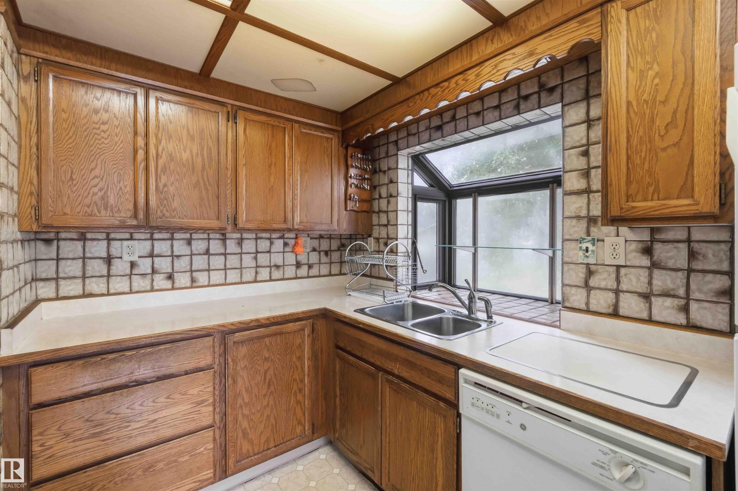 Kitchen featuring wood cabinetry, a double basin stainless steel sink, a tiled backsplash, laminate countertops, and a garden window - 16 Michigan Street, Devon, AB - Indoor Photo Showing Kitchen With Double Sink