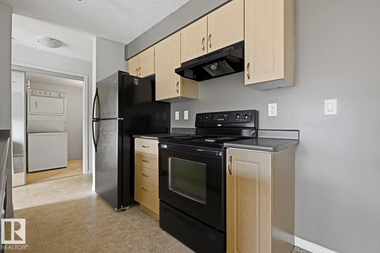 Kitchen featuring light wood-finish cabinetry, black appliances, dark countertops, and tiled flooring - #312 13908 136 St Nw, Edmonton, AB - Indoor Photo Showing Kitchen