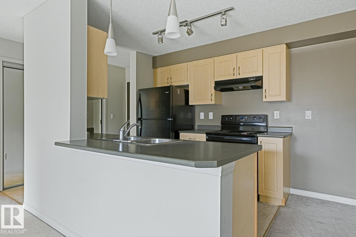 Kitchen area featuring light wood-finish cabinetry, dark countertops, and black appliances - #312 13908 136 St Nw, Edmonton, AB - Indoor Photo Showing Kitchen With Double Sink